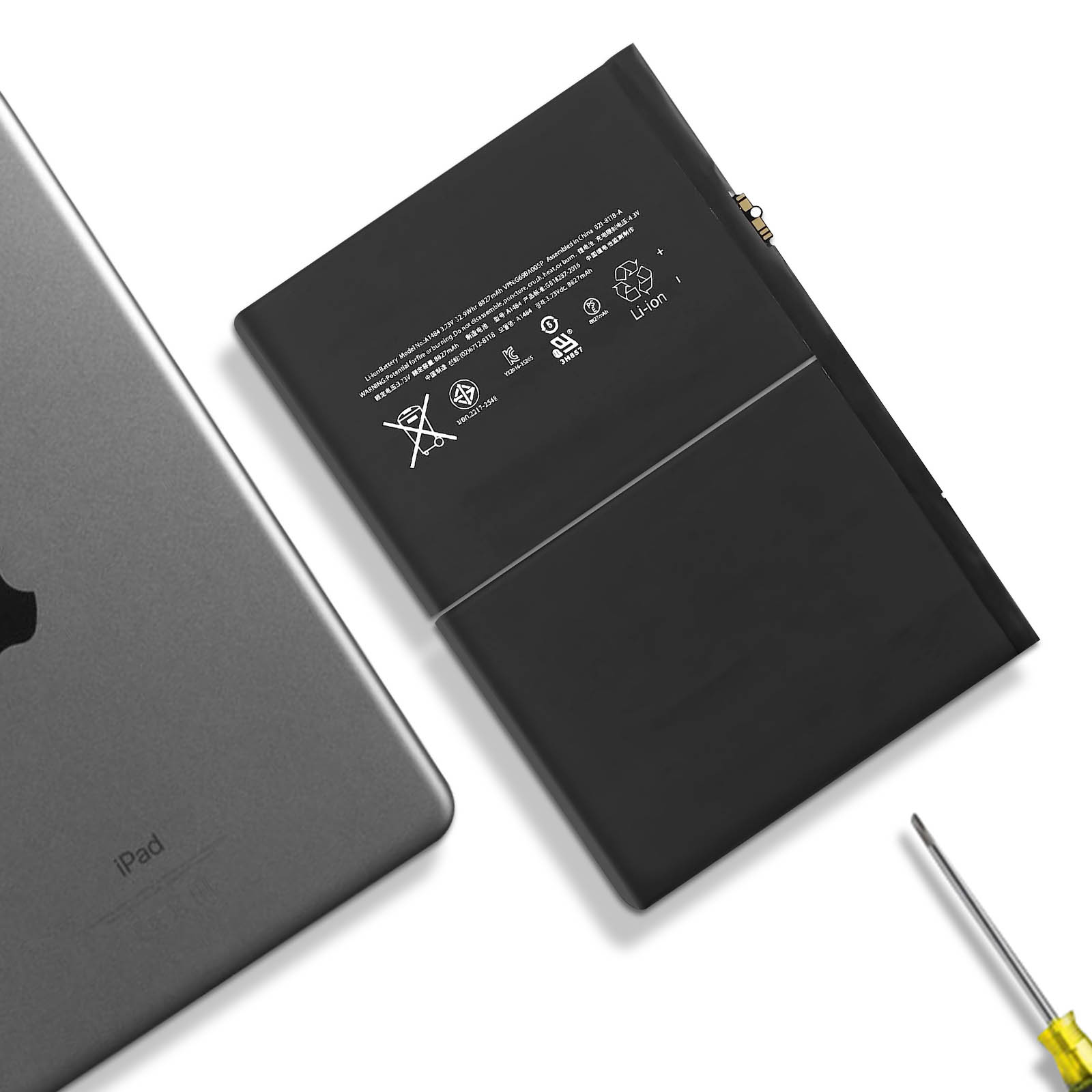 Batería de iPad sobre una superficie blanca. También se ve un destornillador y parte del iPad.
