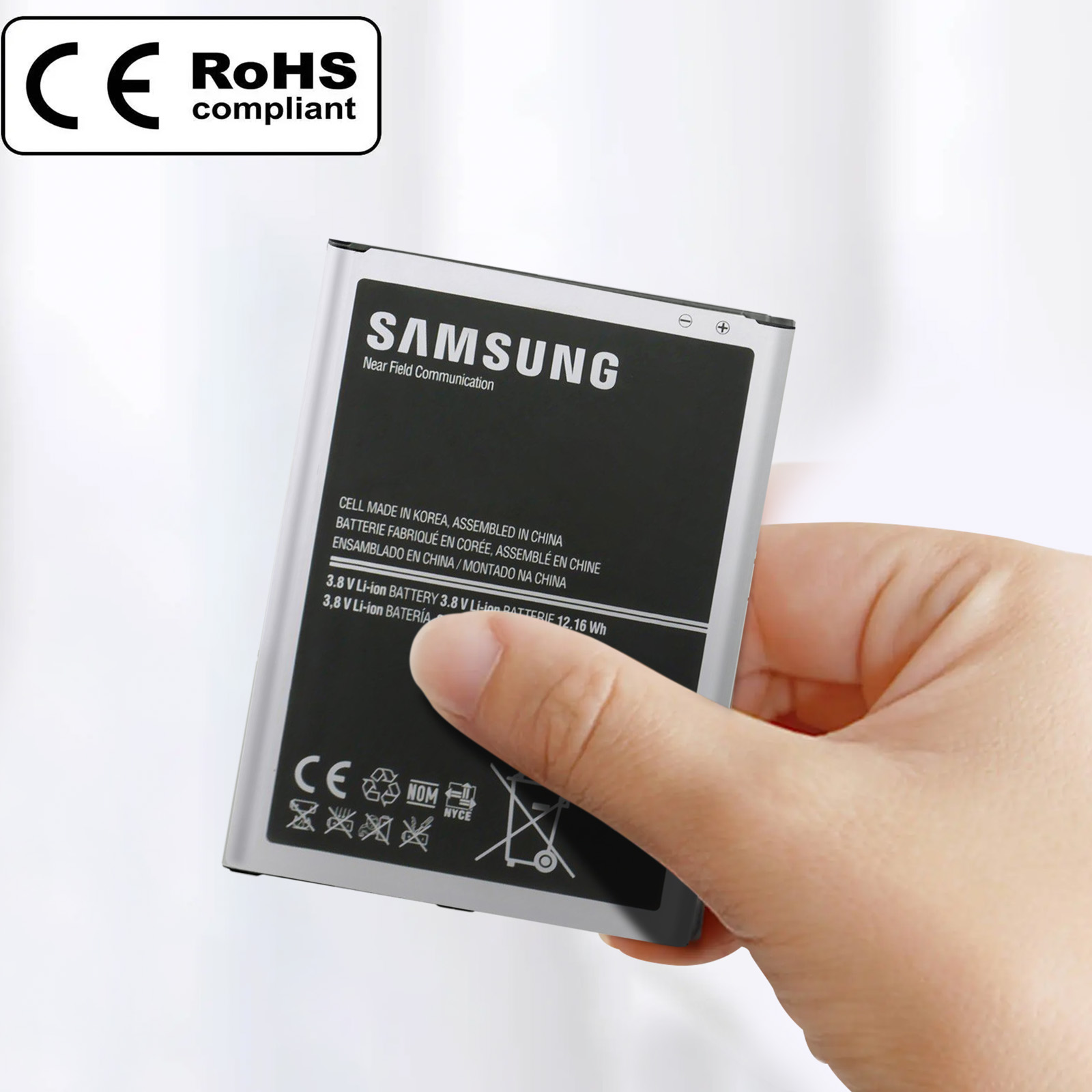Una batería Samsung plateada con texto y logotipos, sostenida por una mano.