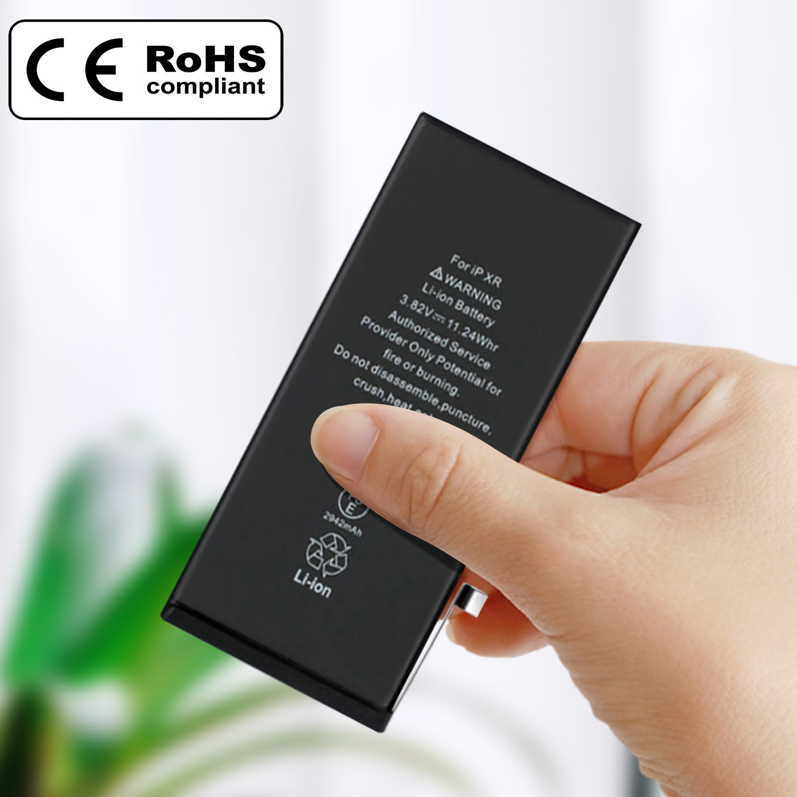 Una mano che tiene una batteria del telefono. La batteria ha testo e un avvertimento. Etichetta conforme RoHS.