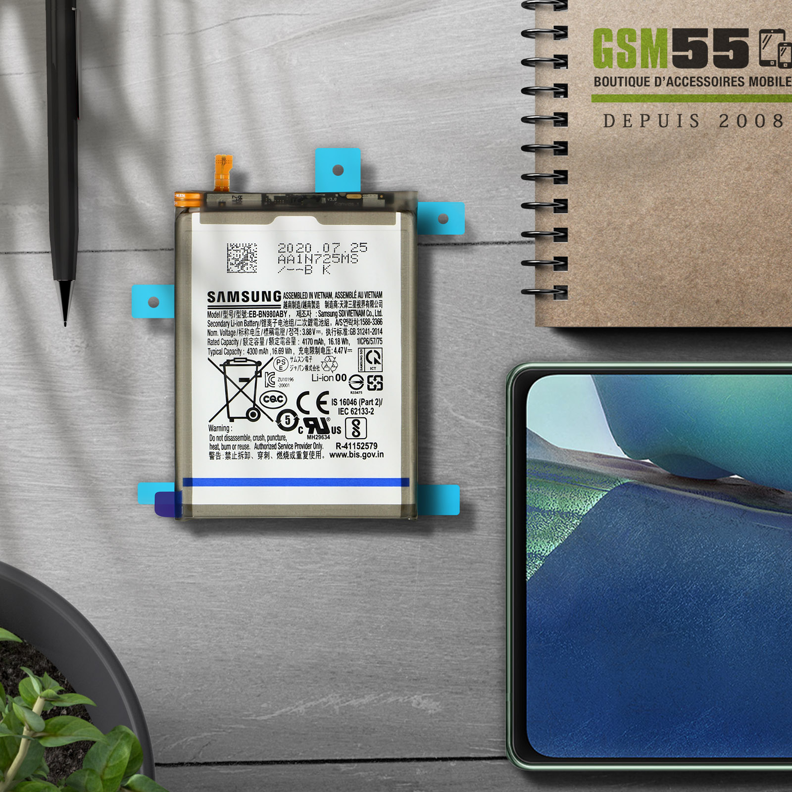 Une batterie de téléphone avec une étiquette dessus, avec un stylo et un carnet à proximité.