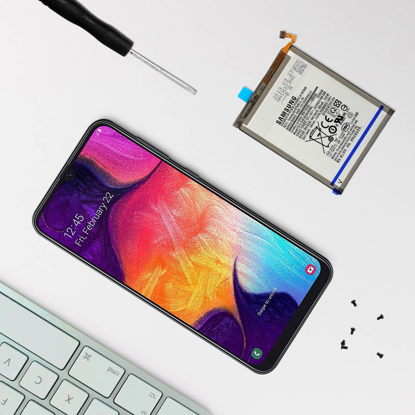 Téléphone, batterie et outils sur surface blanche. L'écran affiche une image colorée.