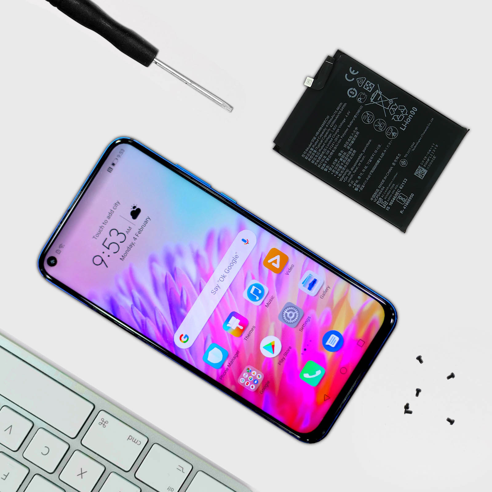 Un telefono smontato con batteria e cacciavite, più una tastiera sulla superficie bianca.