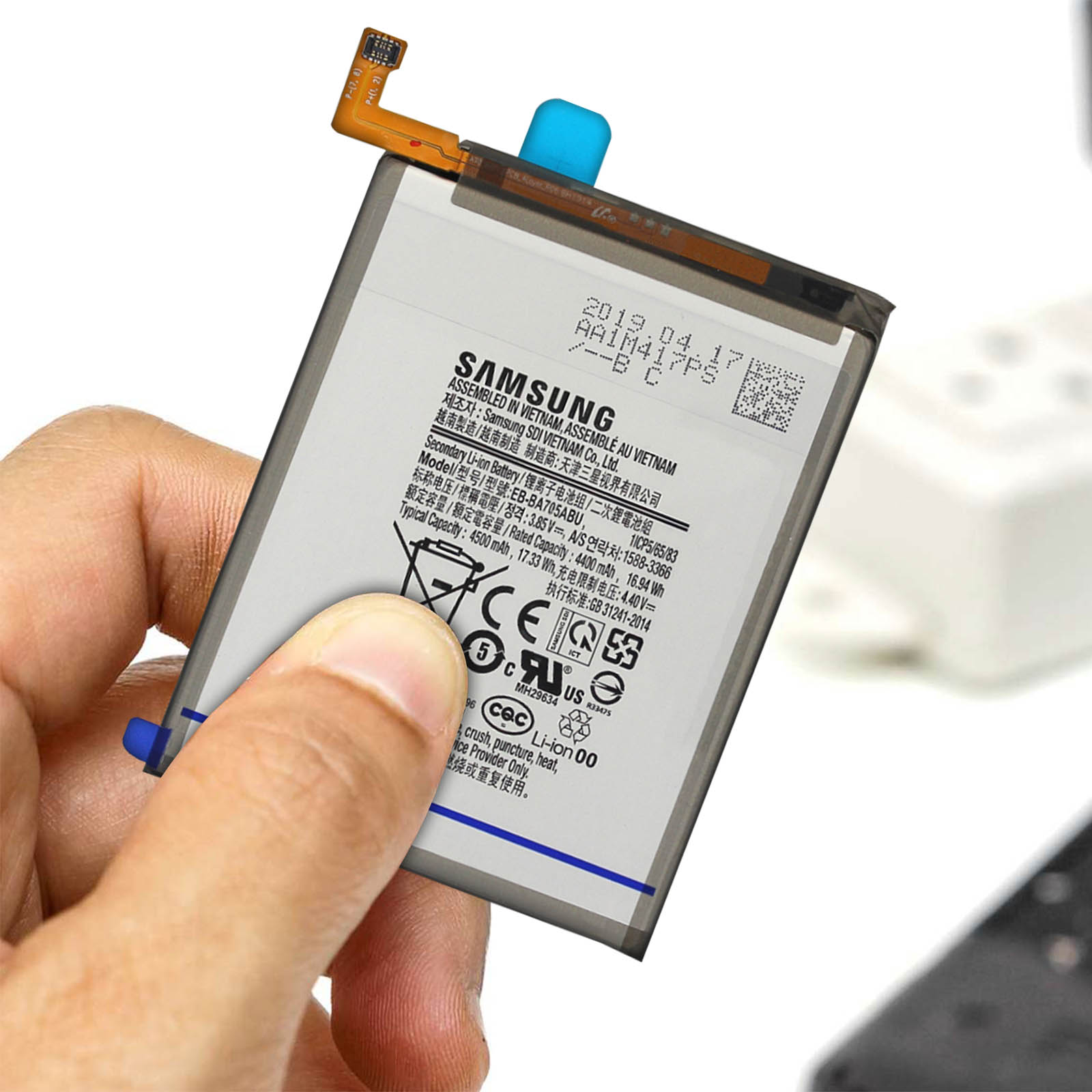 Hand hält eine Samsung-Telefonbatterie mit Etiketten und einem Anschlusskabel.