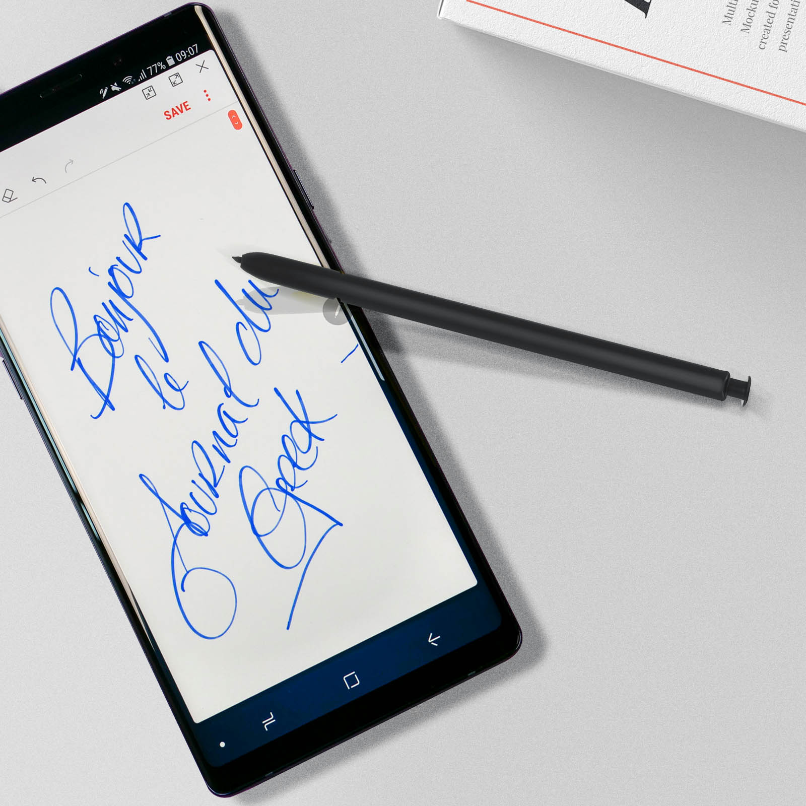 Ein schwarzes Telefon mit einem Stift, der auf den Bildschirm schreibt. Text auf dem Telefon lautet Bonjour le Journal Geek.