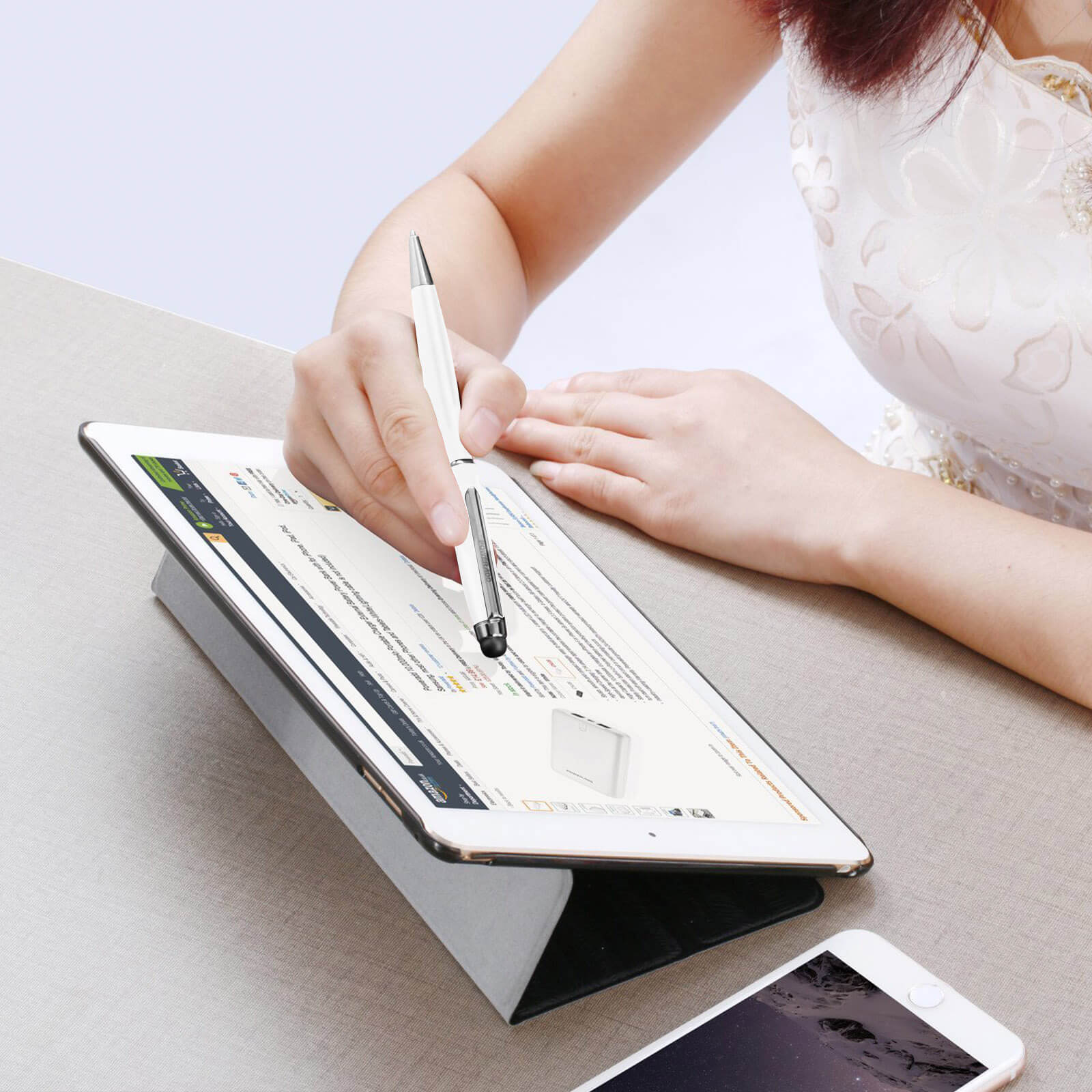 Eine Person, die ein Tablet mit einem Stift benutzt. Das Tablet steht auf einem Ständer, und es liegt ein Telefon in der Nähe.