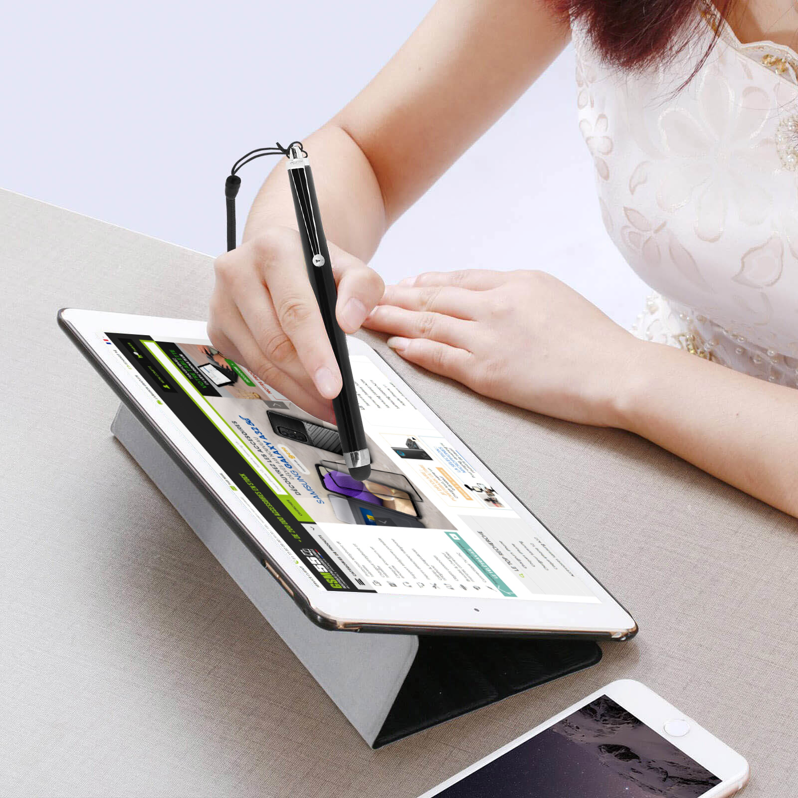 Eine Frau benutzt einen schwarzen Stift auf einem Tablet, das von einem Ständer gehalten wird. Darunter ein Telefon.