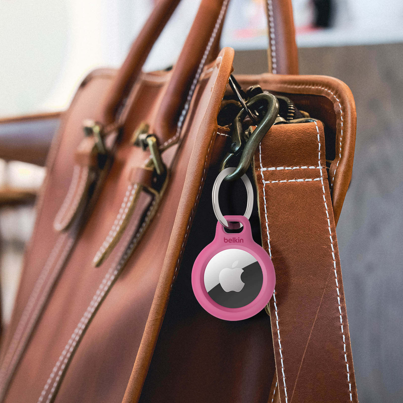Różowy AirTag Belkin na breloczku, przymocowany do brązowej skórzanej torby.