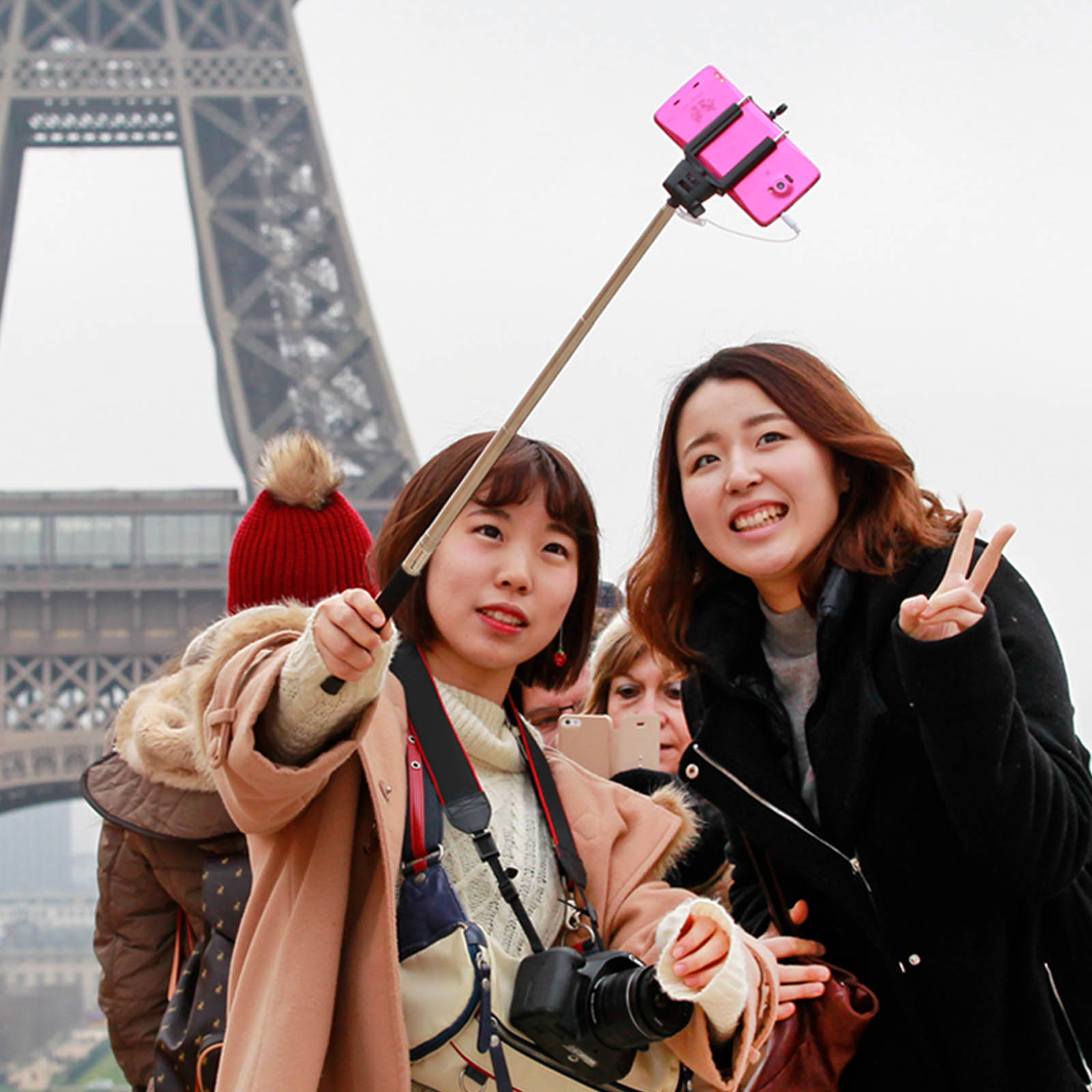 Zwei Frauen und der Eiffelturm, die mit einem rosa Telefon und Selfie-Stick ein Foto machen.