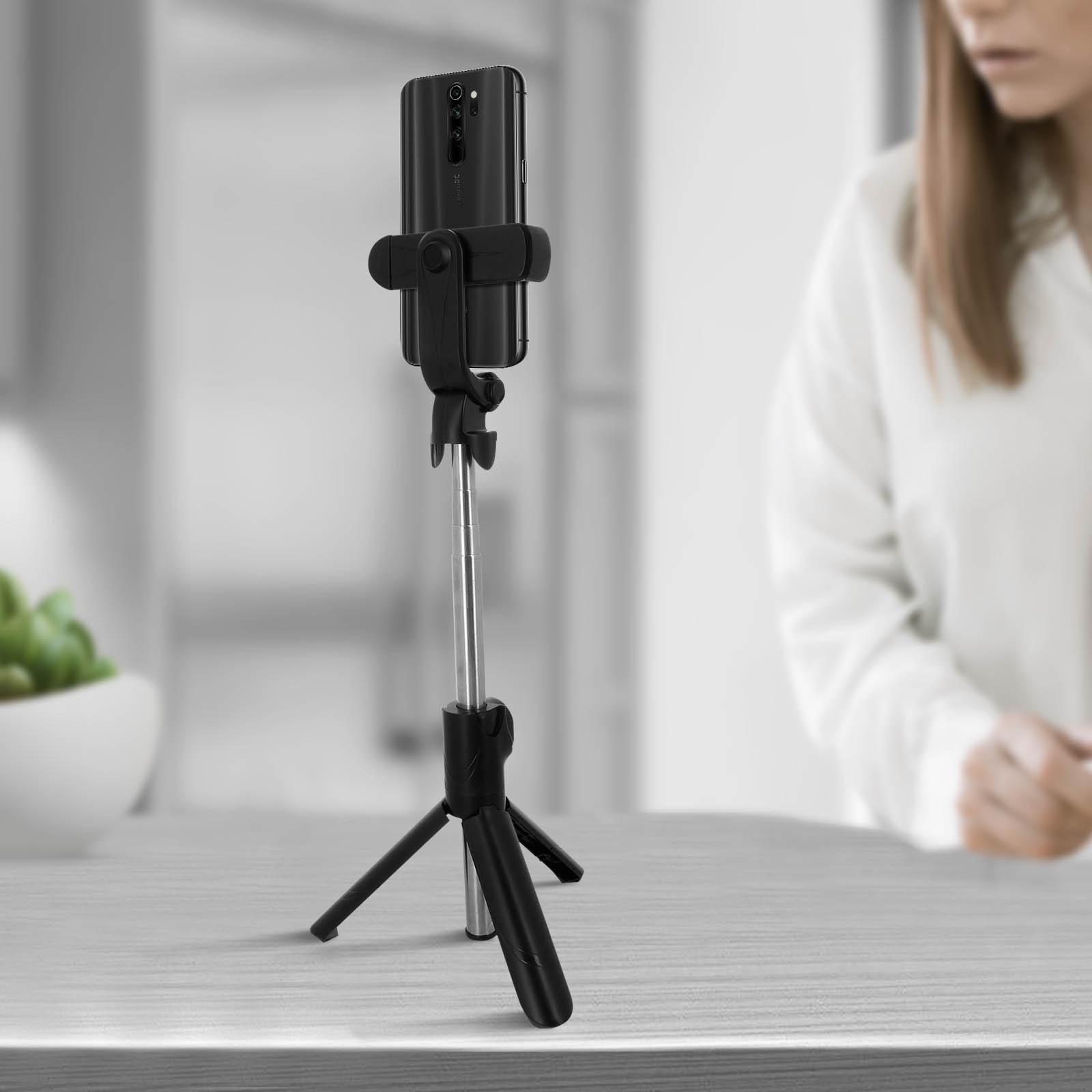 Un bastone per selfie nero con un telefono, su un tavolo, con uno sfondo sfocato.