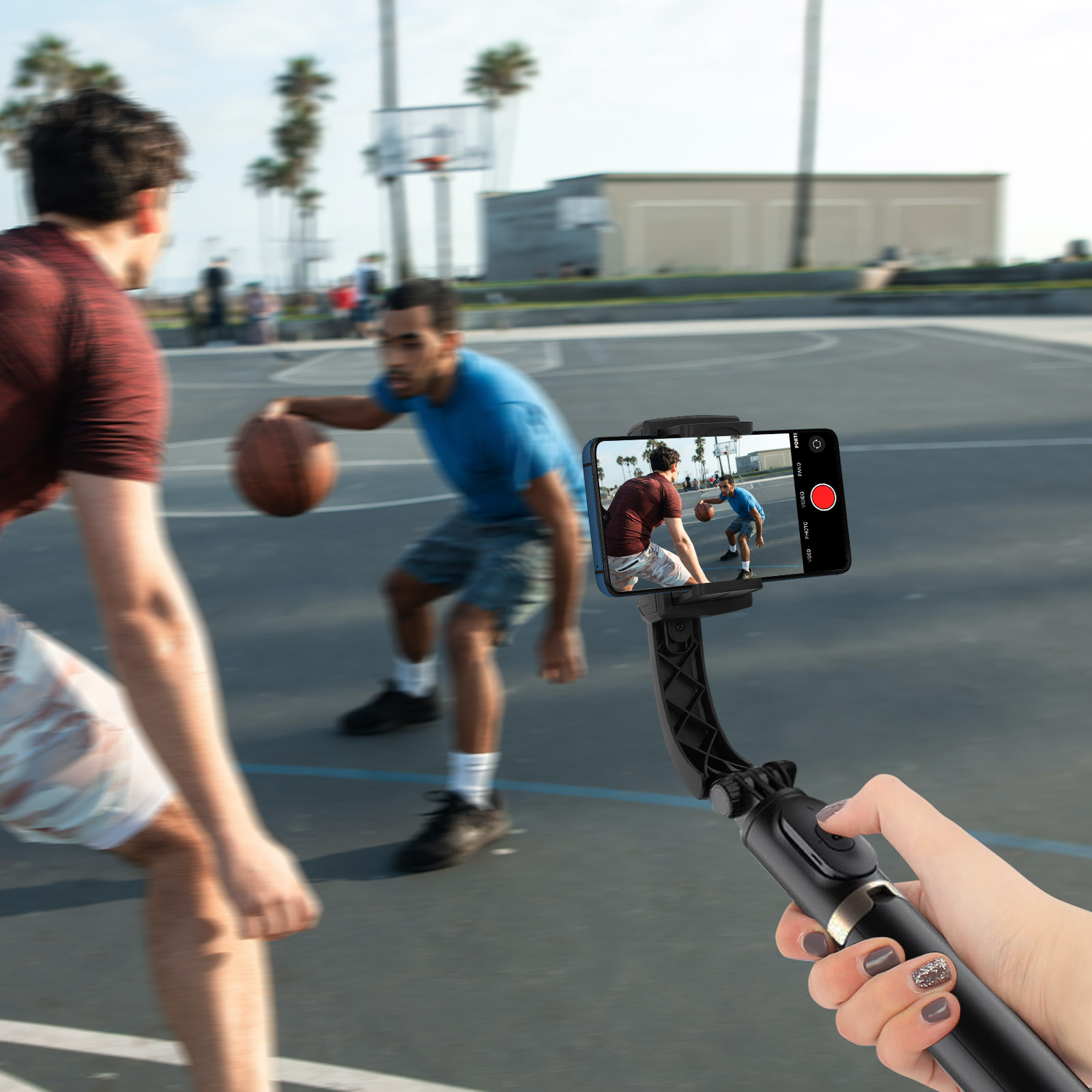 Dos hombres jugando baloncesto, filmados por un teléfono en un palo selfie, en una cancha de baloncesto.