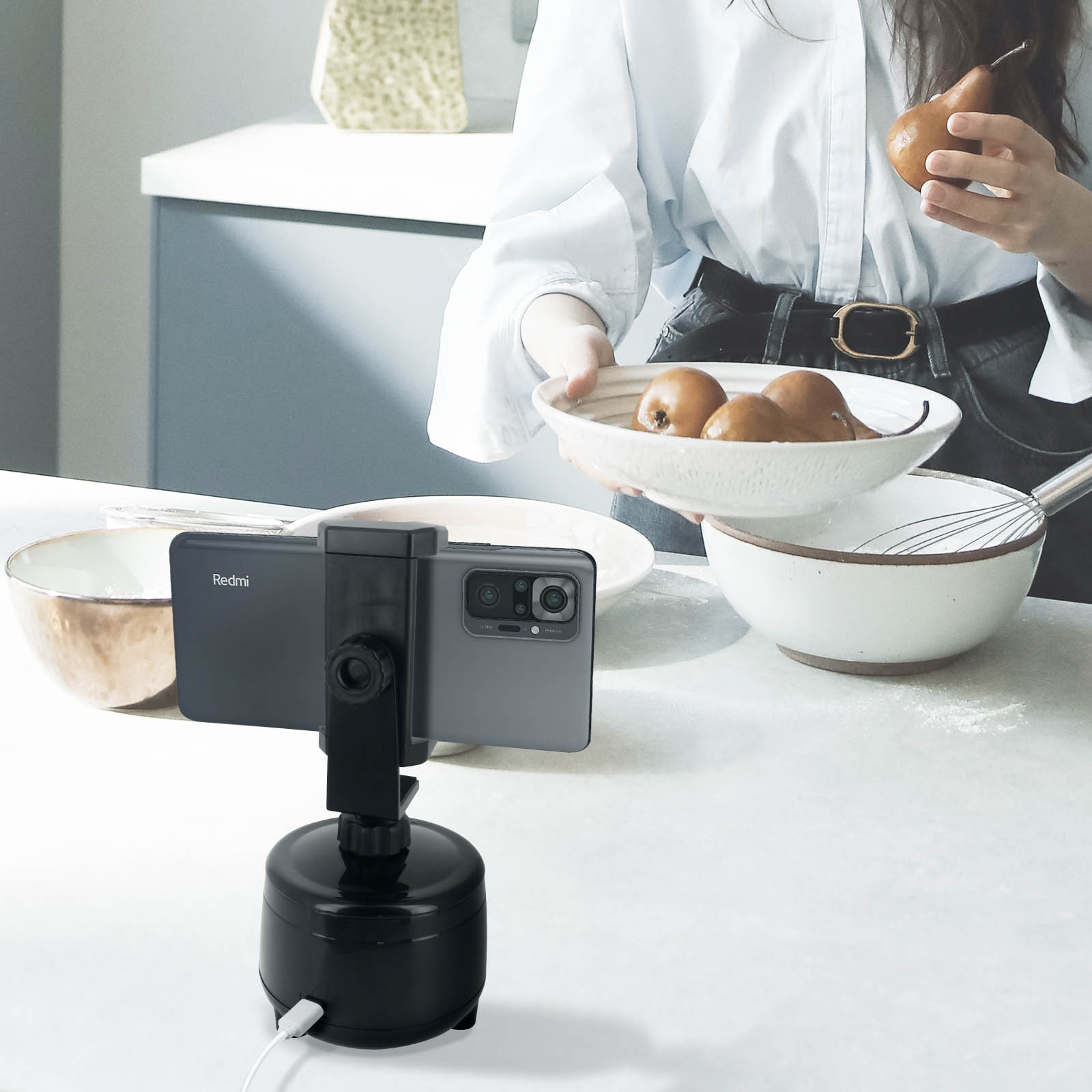 Telefon, der von einem Gimbal gehalten wird und die Zubereitung von Speisen filmt. Küchenumgebung mit Frau im Hintergrund.