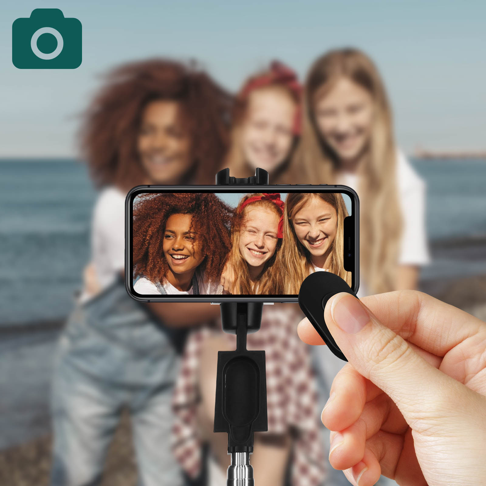 Un palo selfie con un teléfono, sostenido por una mano, con tres mujeres sonriendo a la cámara.