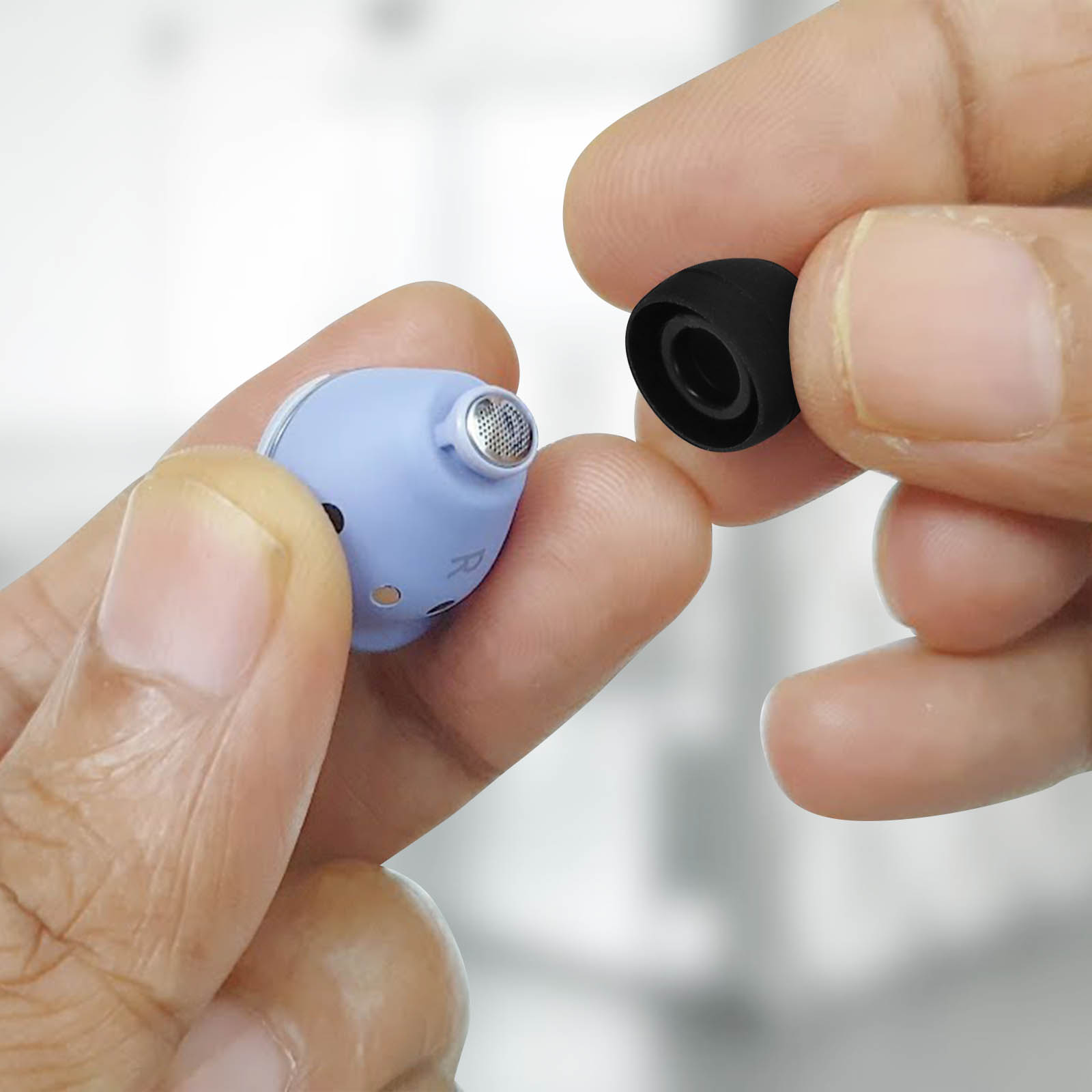 Le mani di una persona che tiene un auricolare blu e un gommino nero. Primo piano, sfondo bianco.