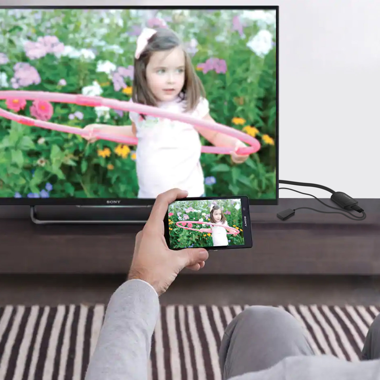 Una persona tiene in mano un telefono che rispecchia lo schermo TV con una bambina con un hula hoop.