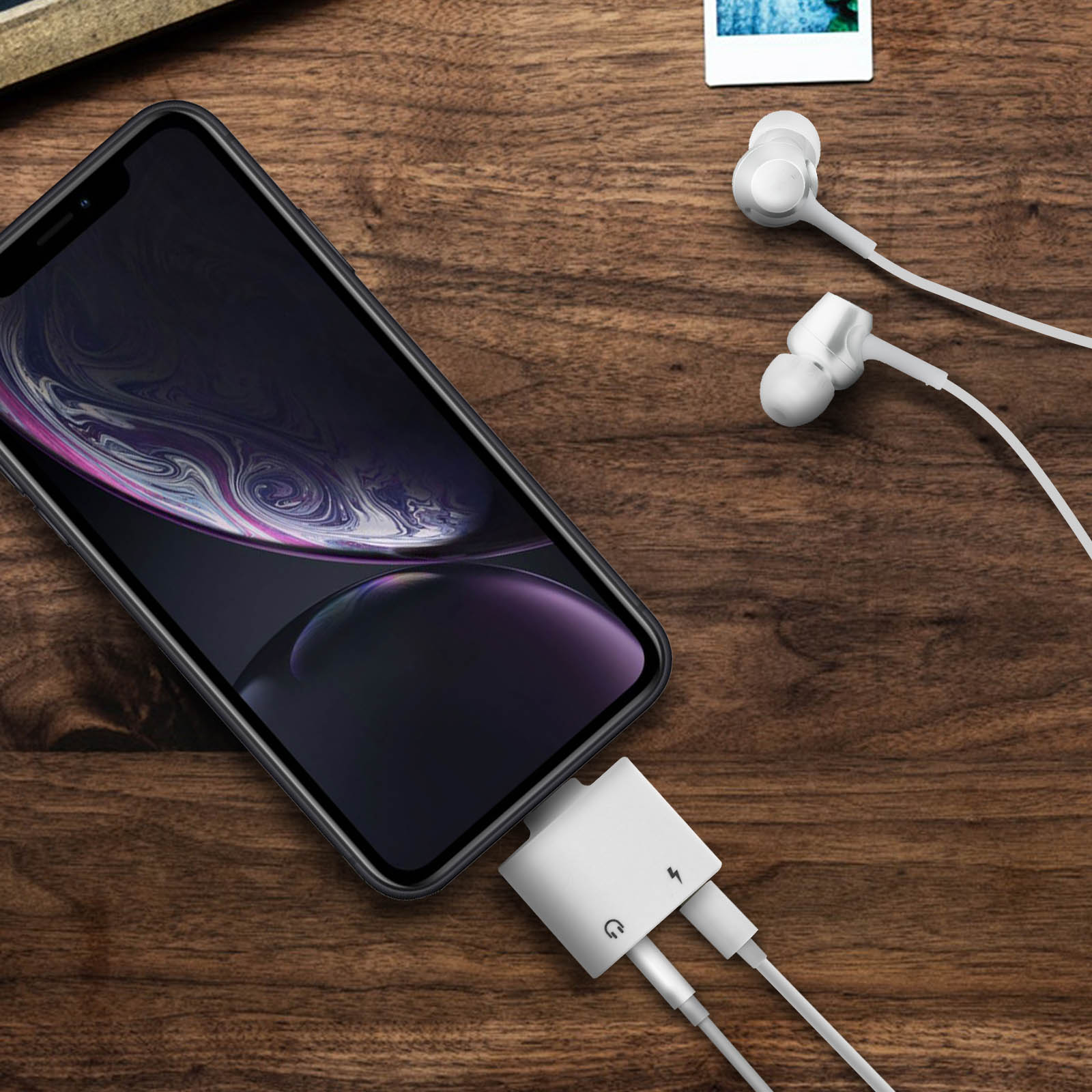 Un téléphone connecté à un adaptateur blanc, avec des écouteurs branchés. Fond de table en bois.