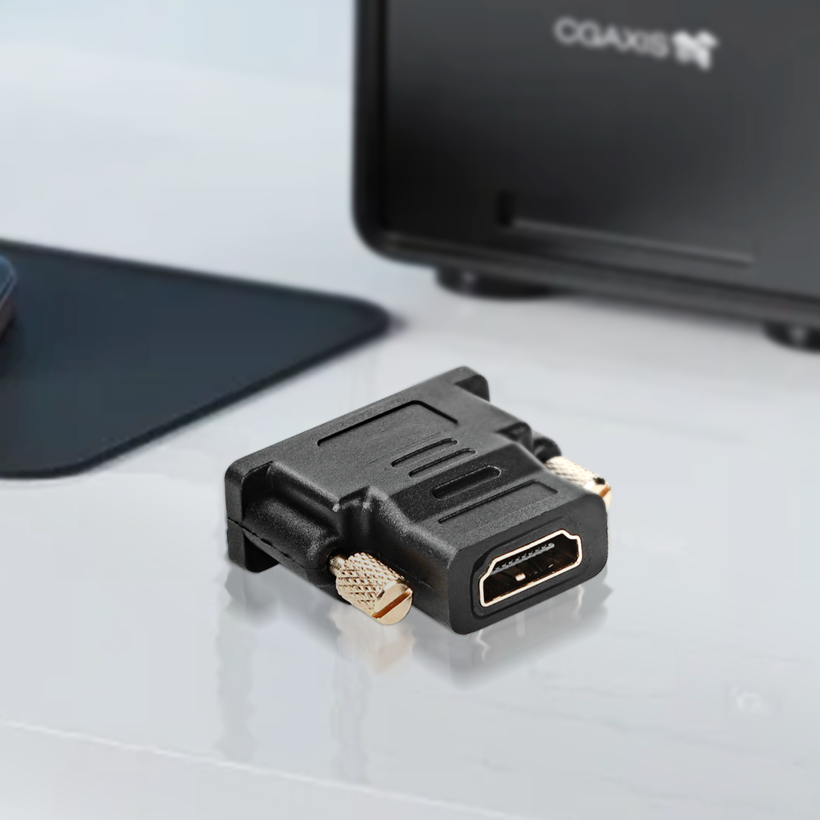 Un adattatore da HDMI a DVI nero su una superficie bianca, con un monitor sullo sfondo.