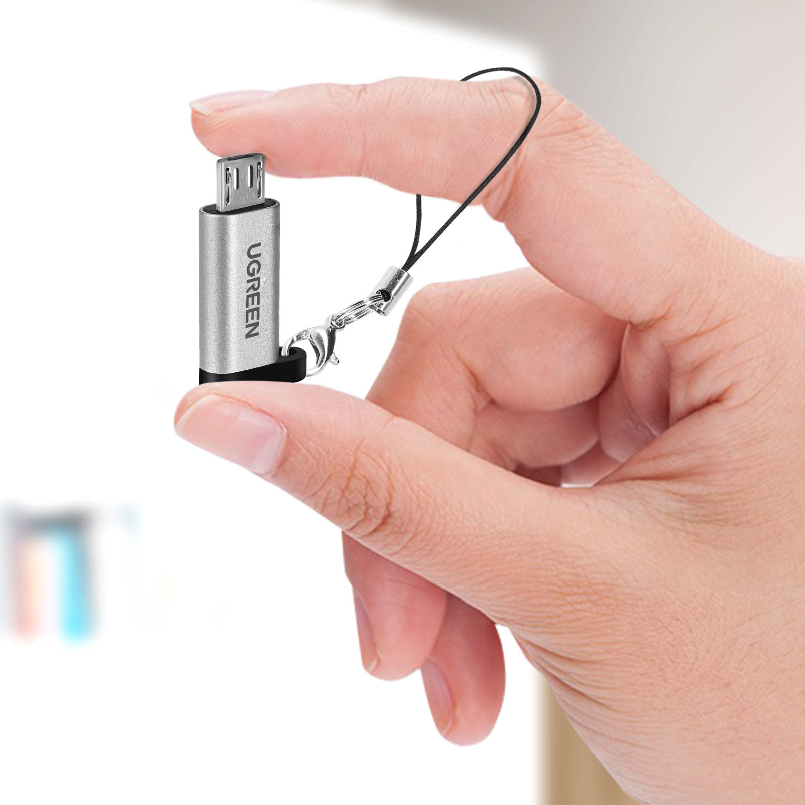 Srebrny adapter UGREEN trzymany w dłoni. Dołączona czarna smycz.