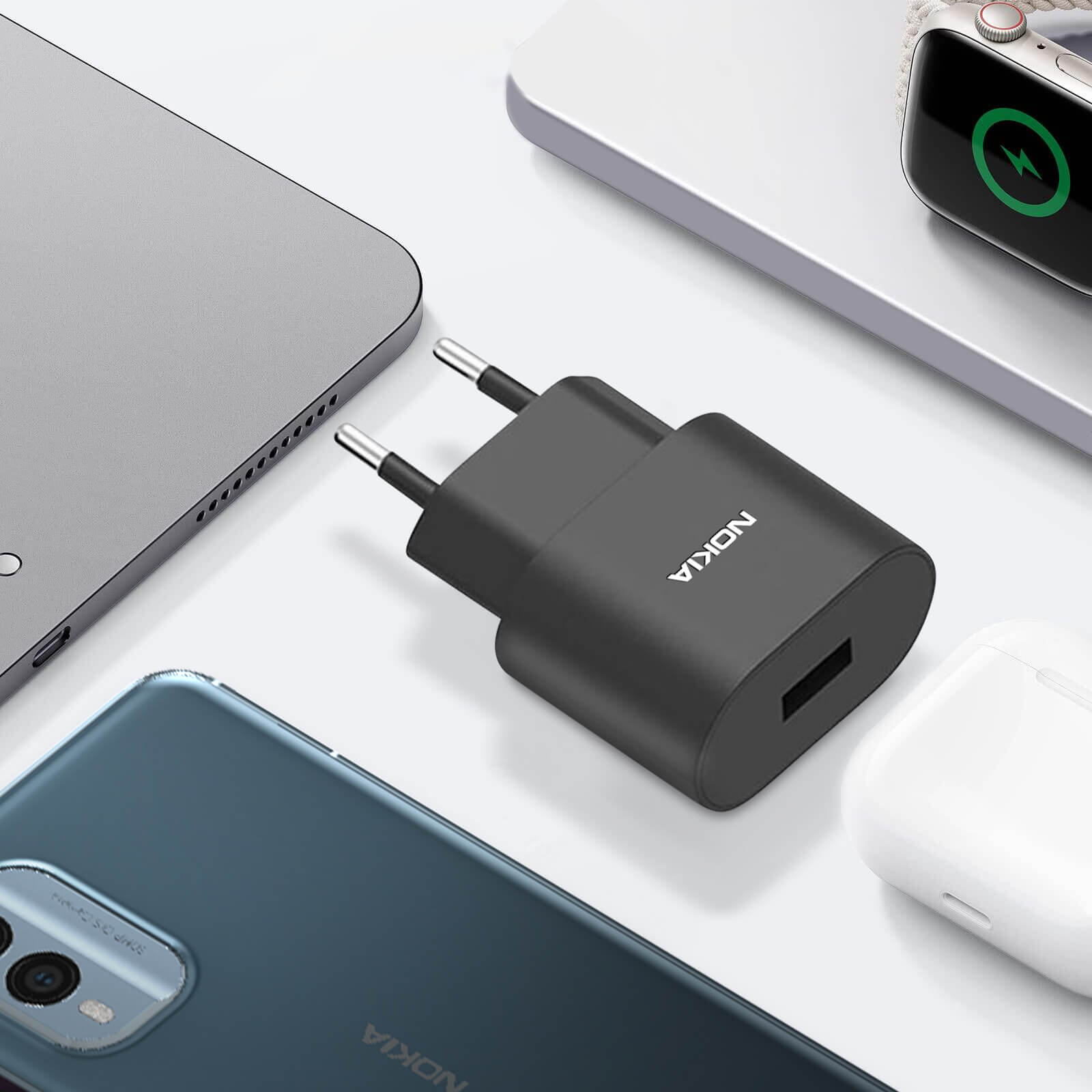 Un chargeur Nokia noir avec un port USB, à côté d'un téléphone, d'écouteurs et d'un ordinateur portable.