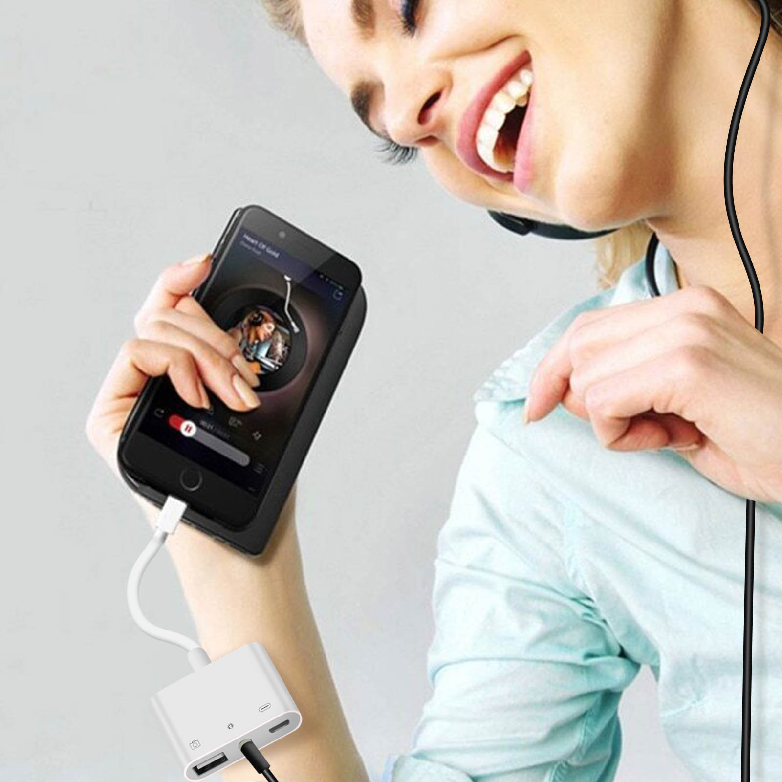 Femme avec casque, tenant un téléphone avec adaptateur. Le téléphone joue de la musique. L'adaptateur a des ports USB et Lightning.