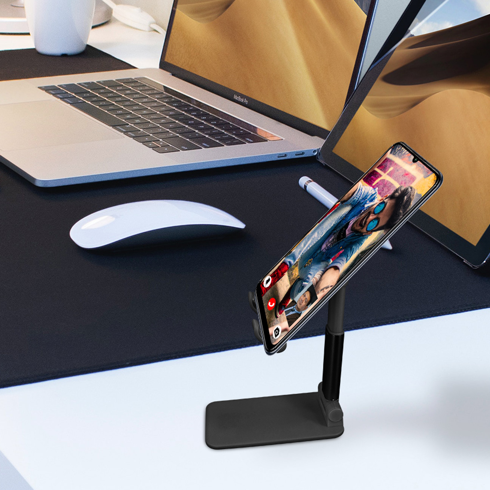 Un telefono su un supporto che mostra la foto di una persona. Laptop e tablet sullo sfondo.