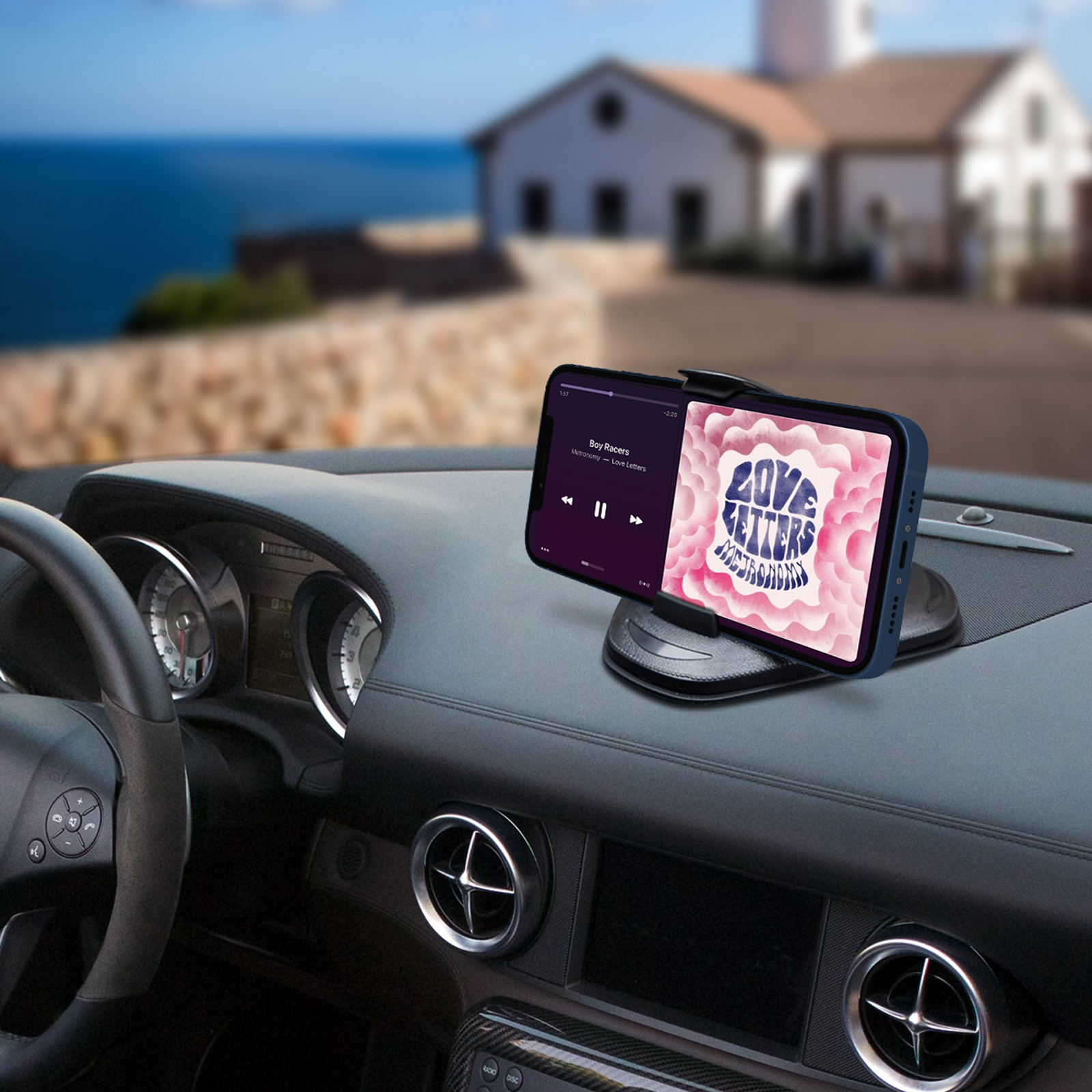 Telefono sul cruscotto, riproduce musica. Vista mare e casa sullo sfondo.