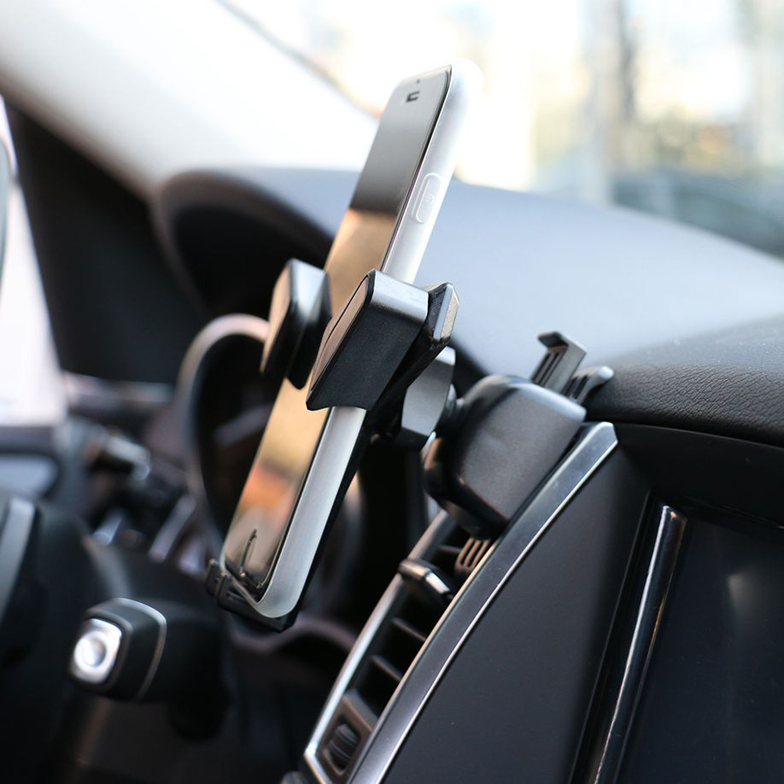 Telefon an Lüftung im Auto montiert, schwarzer Innenraum. Telefon ist vertikal ausgerichtet.