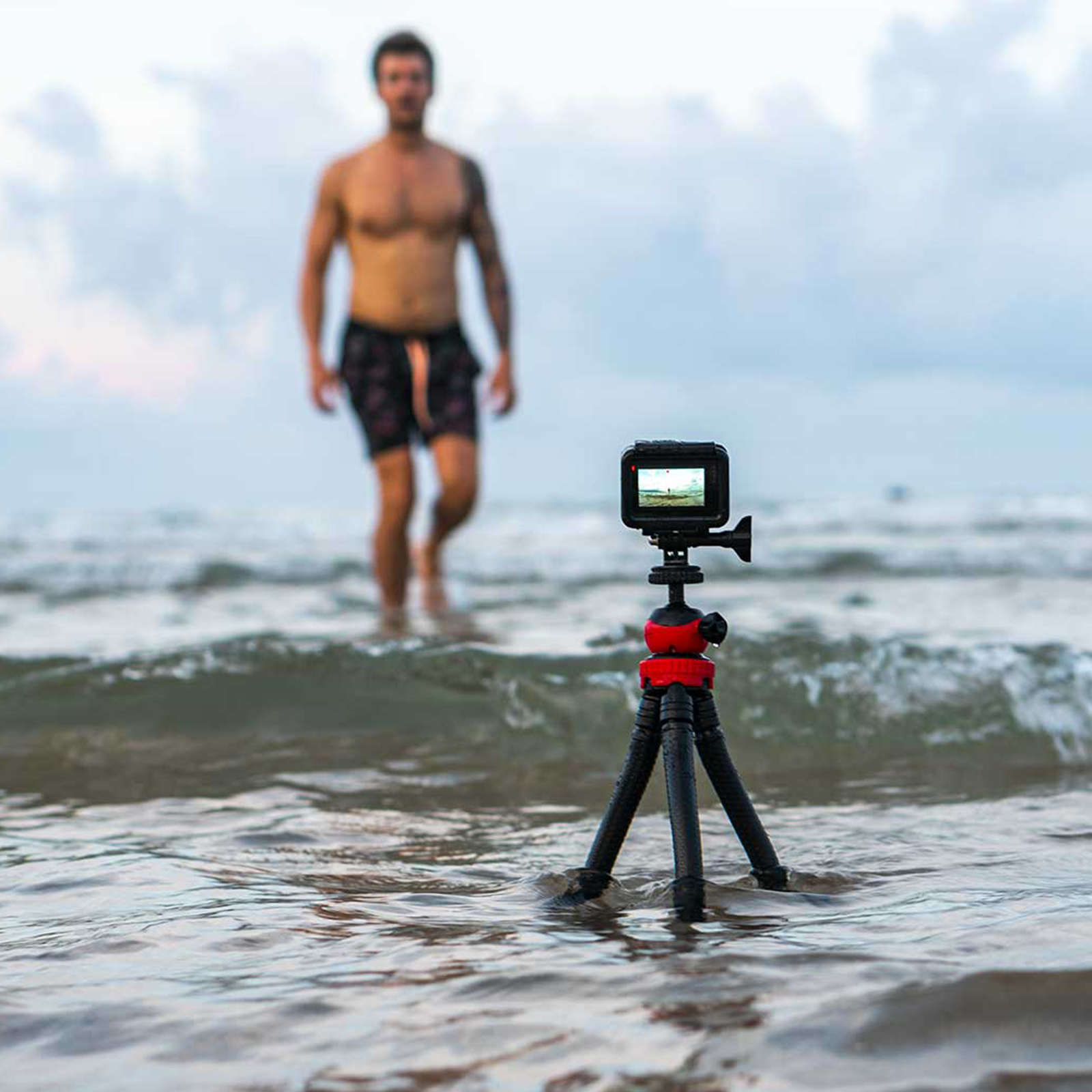 Un uomo in mare cammina dietro un treppiede con una fotocamera che registra le onde.