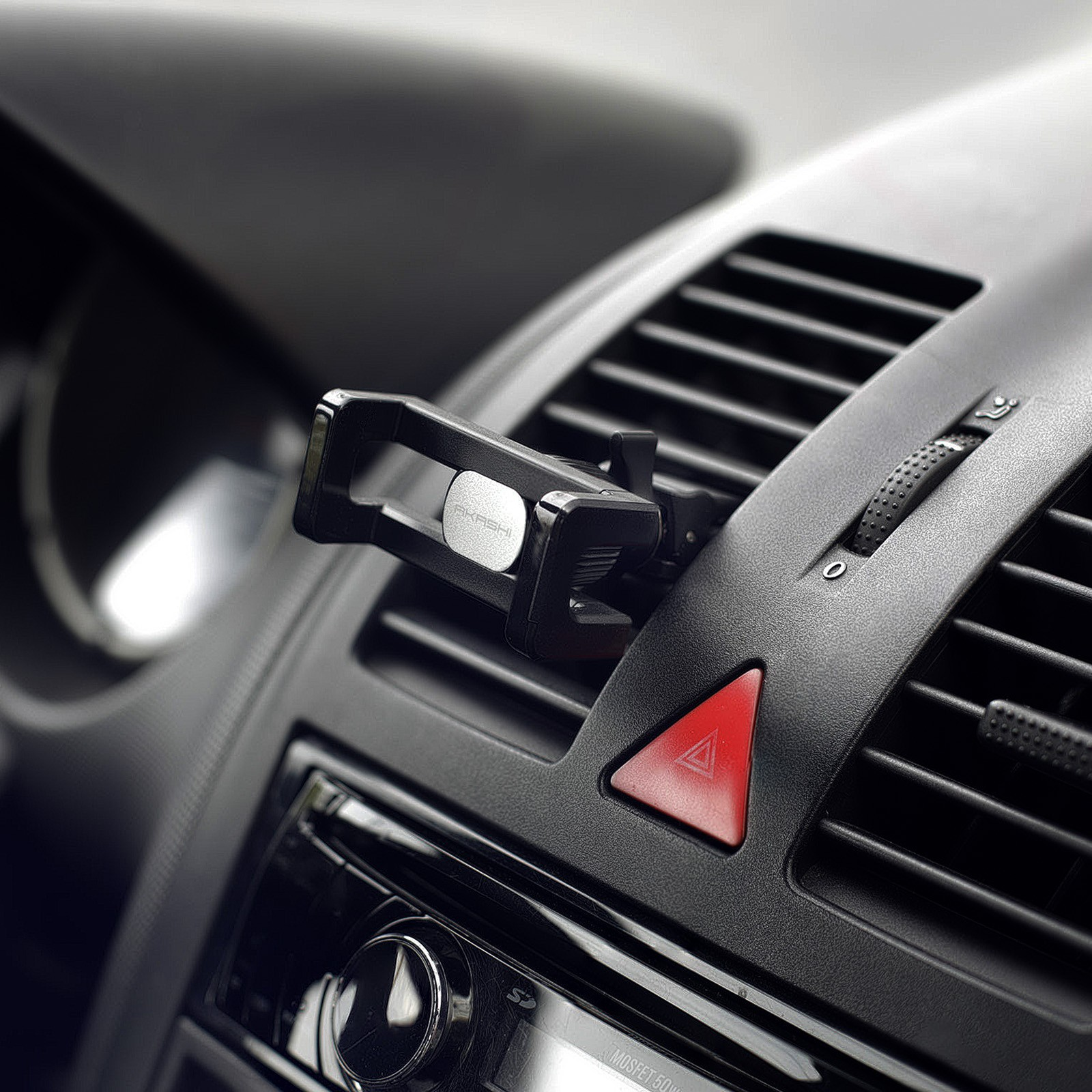 Schwarzer Telefonhalter in einer Lüftung im Auto installiert, mit rotem Warnblinklicht-Knopf im Hintergrund sichtbar.
