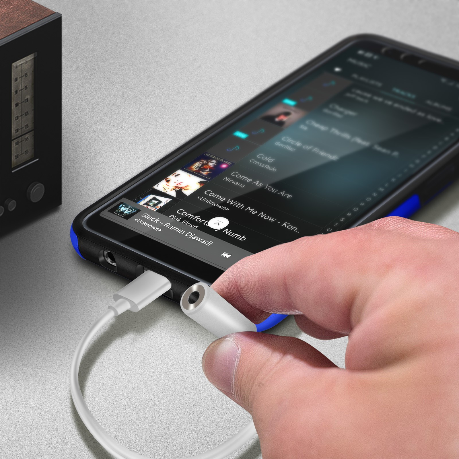 Una mano conecta un adaptador blanco con un conector para auriculares a un teléfono. El teléfono reproduce música.