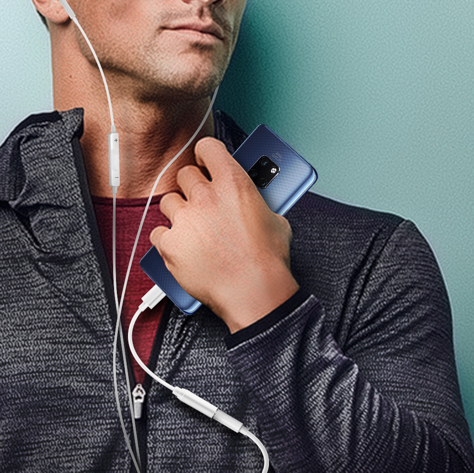 Un hombre sosteniendo un teléfono con auriculares. El teléfono es azul y el fondo es una pared verde azulado.