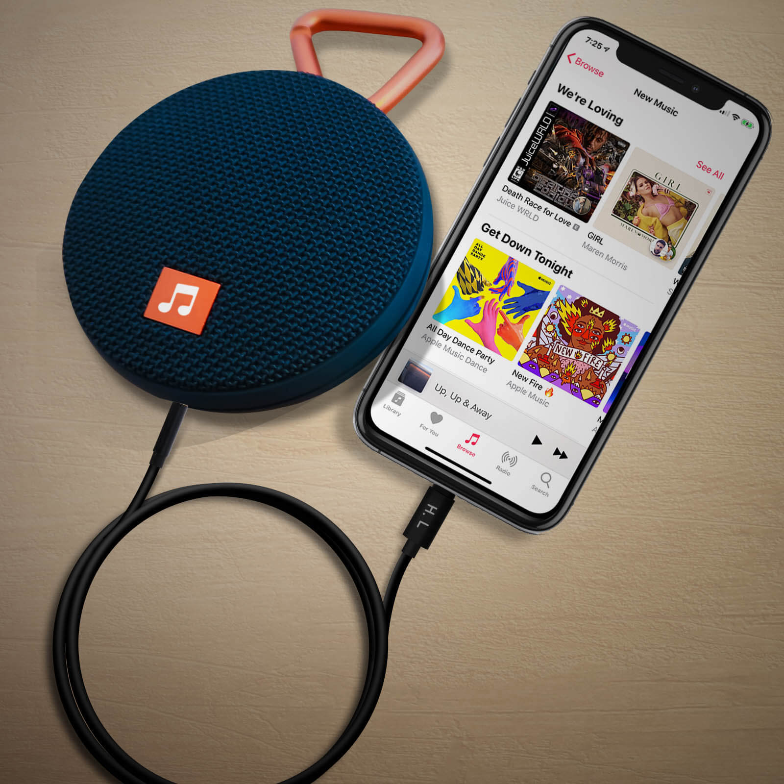 Altavoz azul con acento naranja, conectado a un teléfono con música, sobre una superficie de madera.