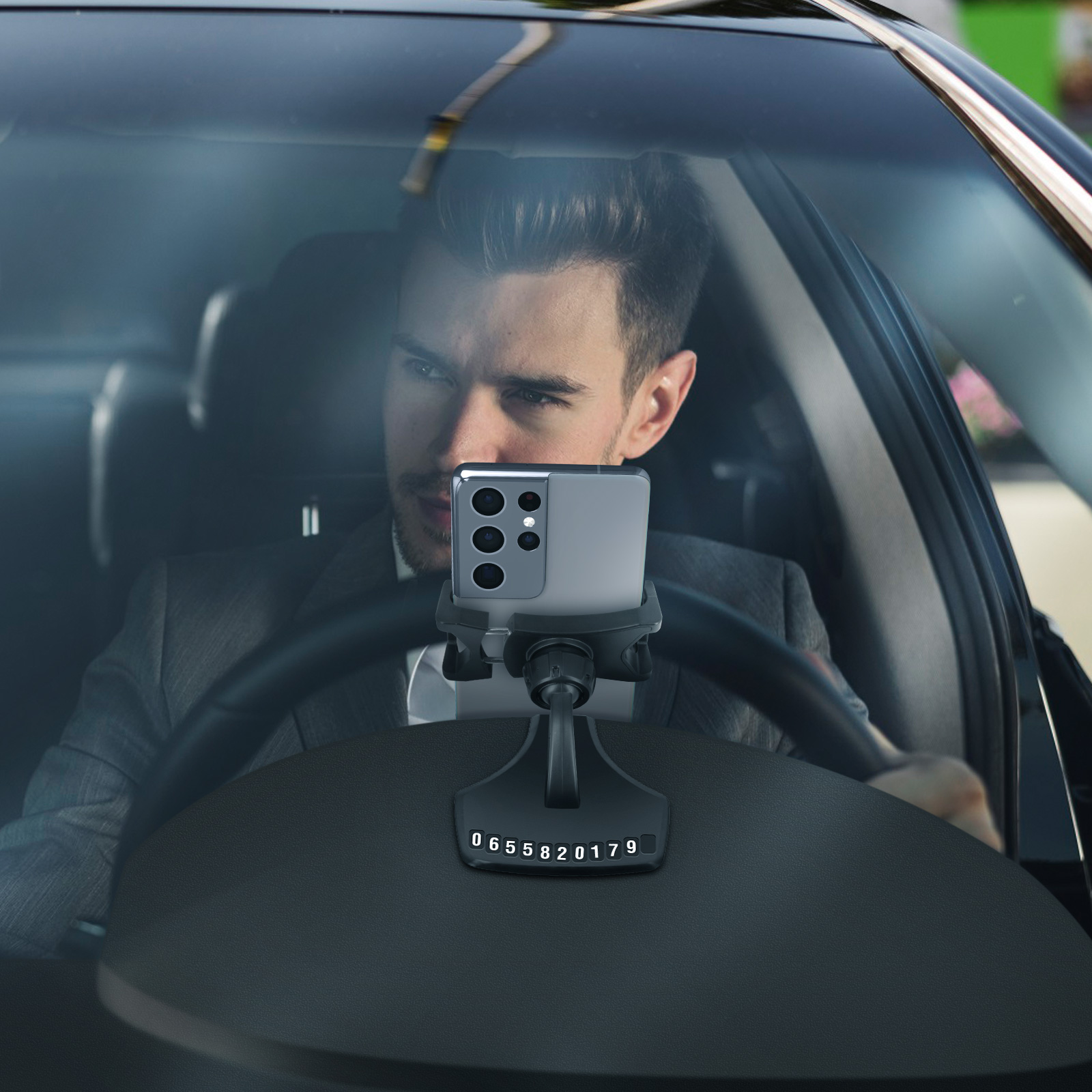 Uomo in giacca e cravatta usa telefono montato sul cruscotto. Il telefono mostra numeri. Volante visibile.