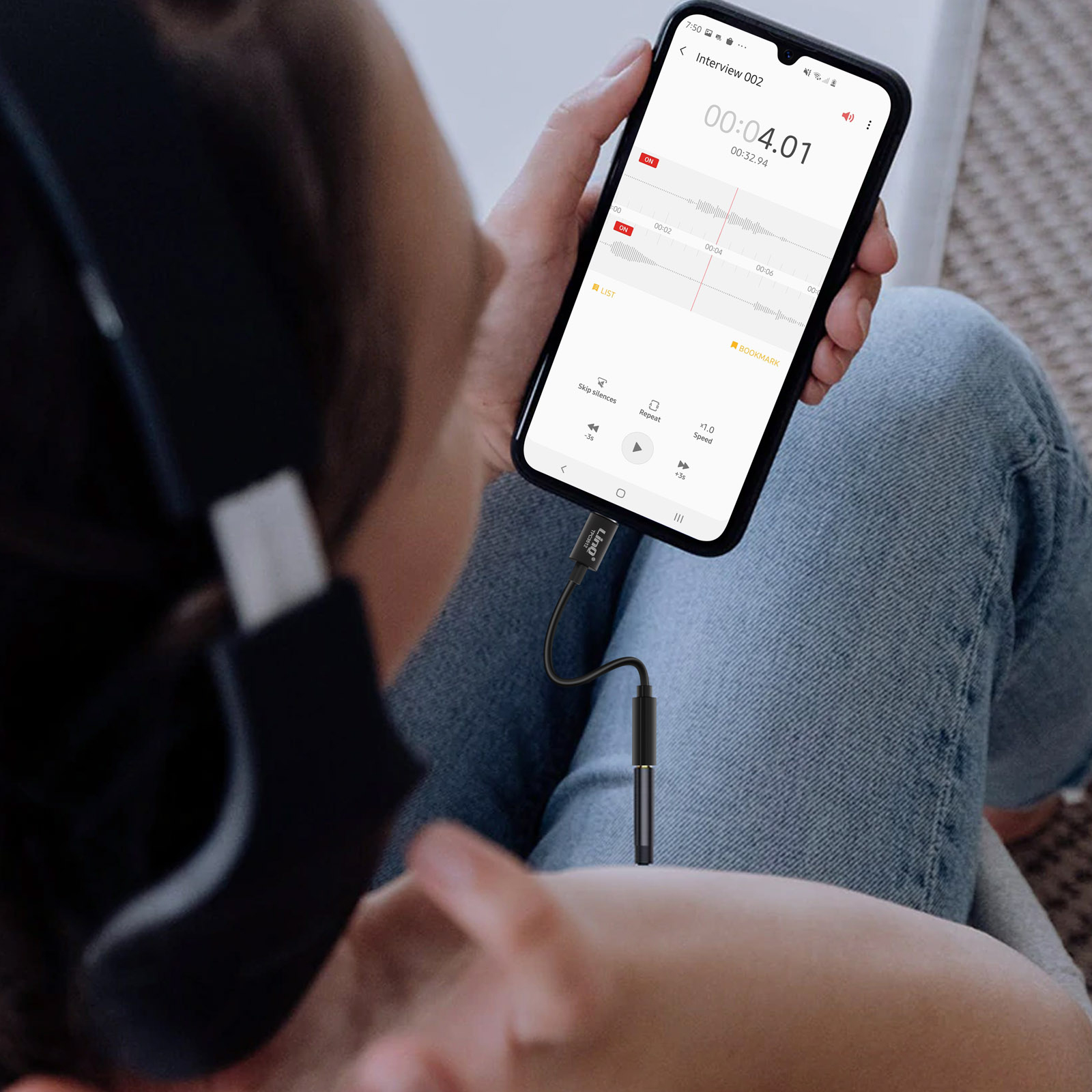 Persona con telefono con interfaccia di registrazione, collegato a cuffie tramite cavo nero.