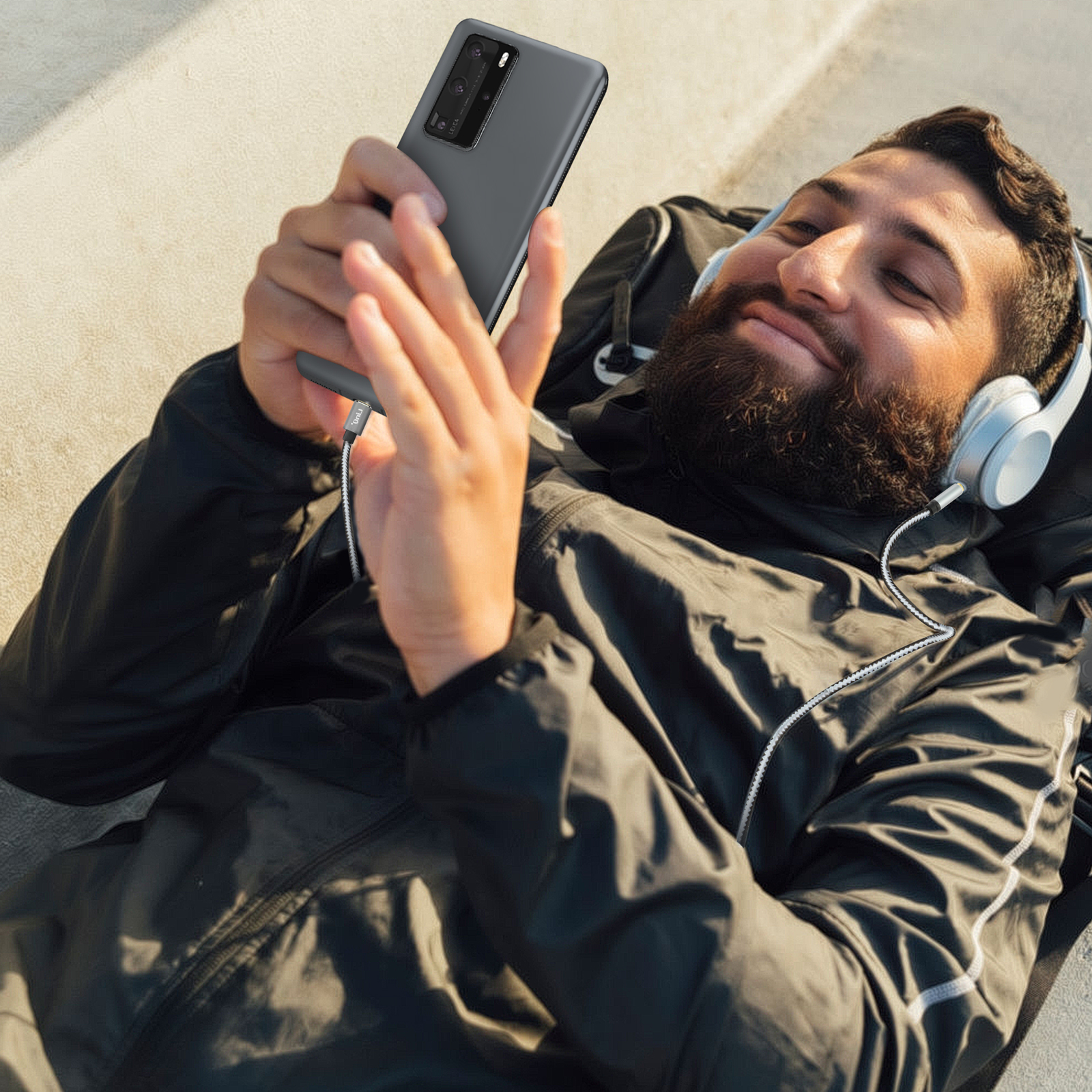 Hombre acostado, sosteniendo un teléfono y con auriculares. El fondo es un día soleado.