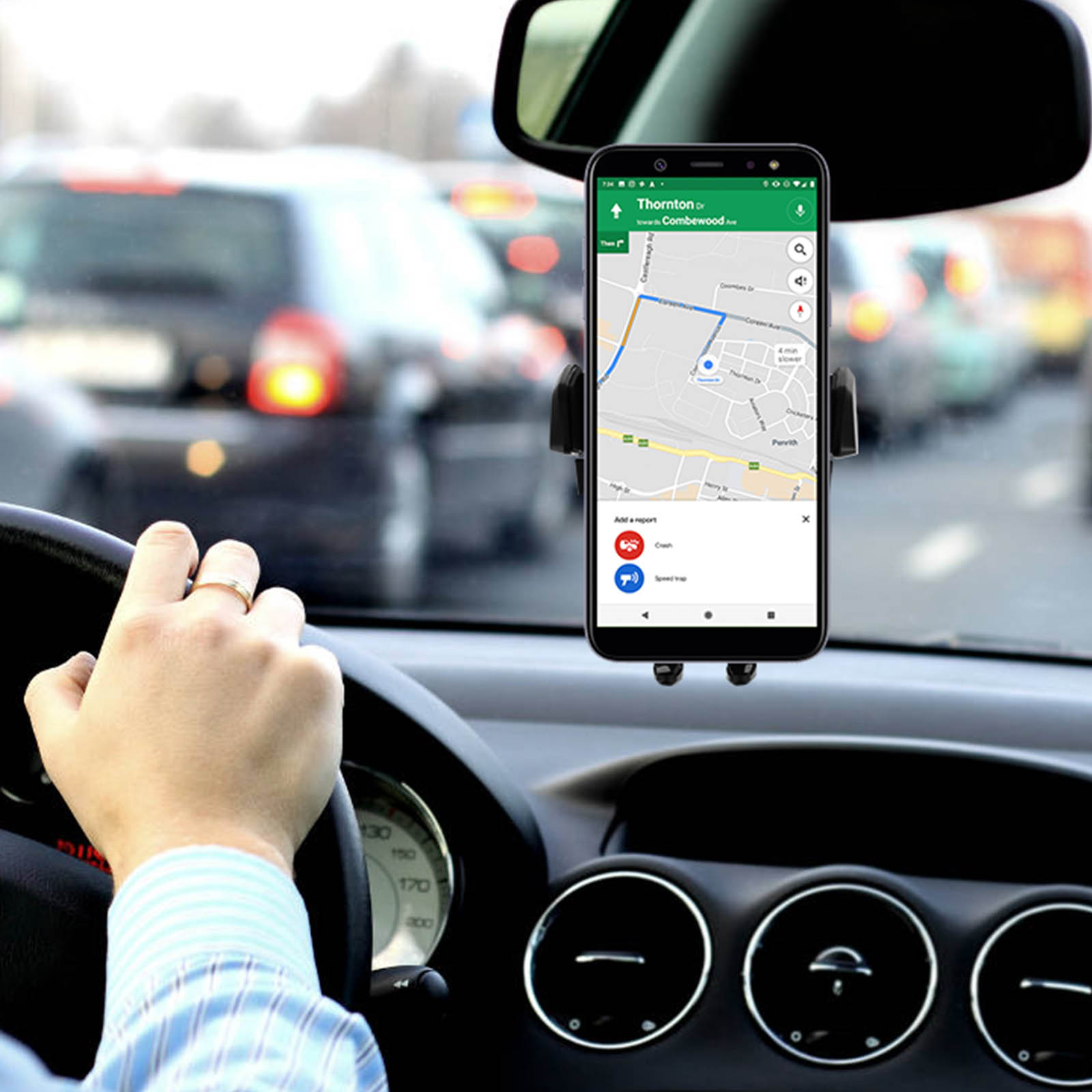 Ein Telefon in einer Autohalterung, das eine Navigations-App anzeigt. Die Hand hält das Lenkrad. Verschwommener Hintergrund.