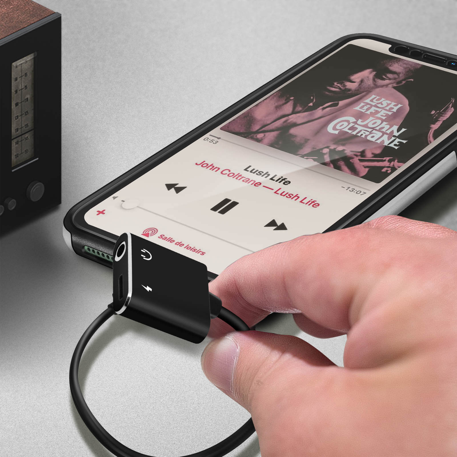 Eine Hand, die ein Telefon hält, das mit einem Adapter verbunden ist. Das Telefon zeigt einen Musikplayer.