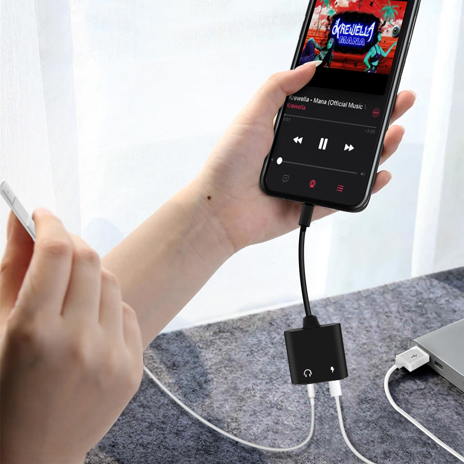 Eine Person hält ein Telefon, das mit einem schwarzen Adapter mit angeschlossenem Headset und USB-Kabel verbunden ist.