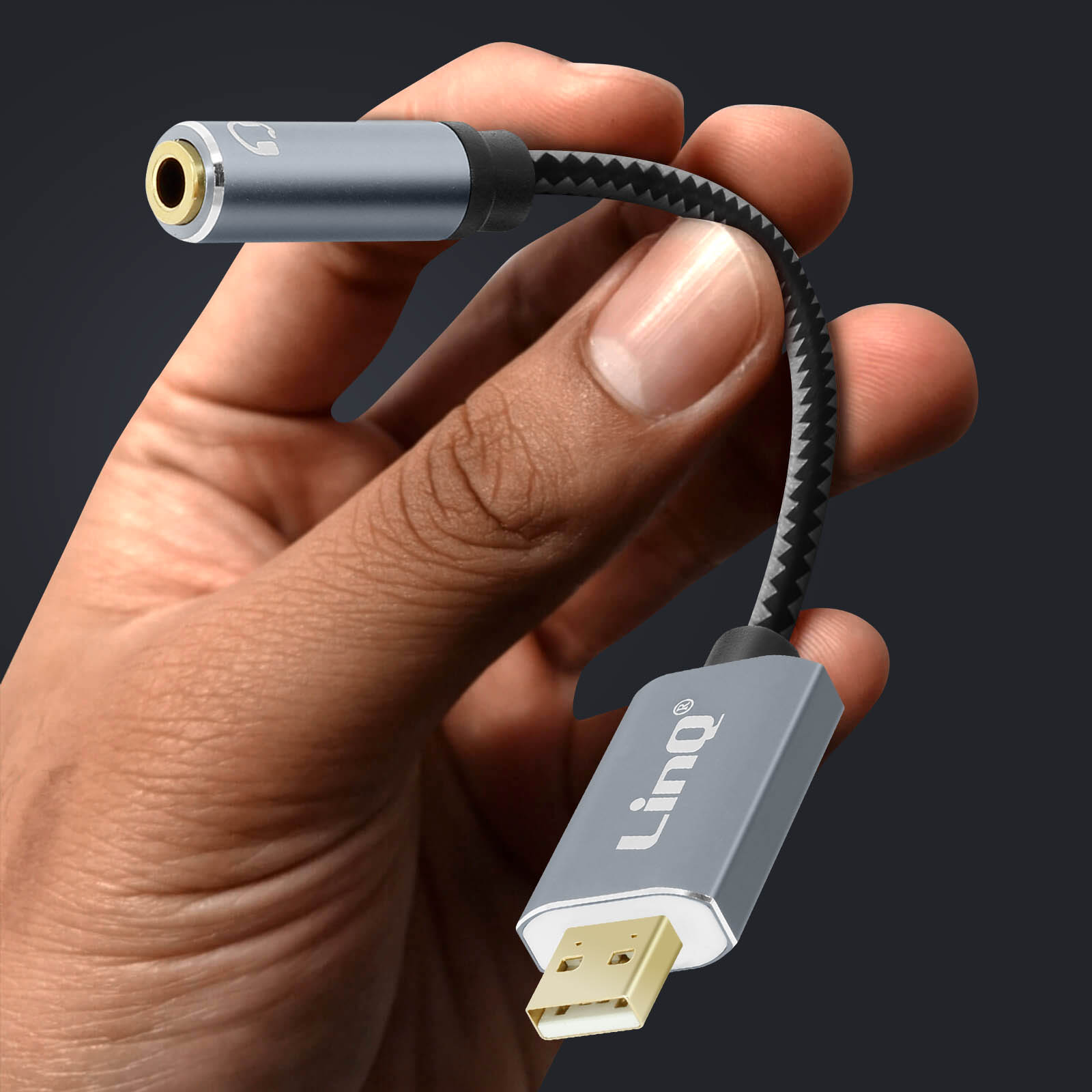 La mano di una persona che tiene un cavo adattatore audio grigio e nero con USB e jack aux.
