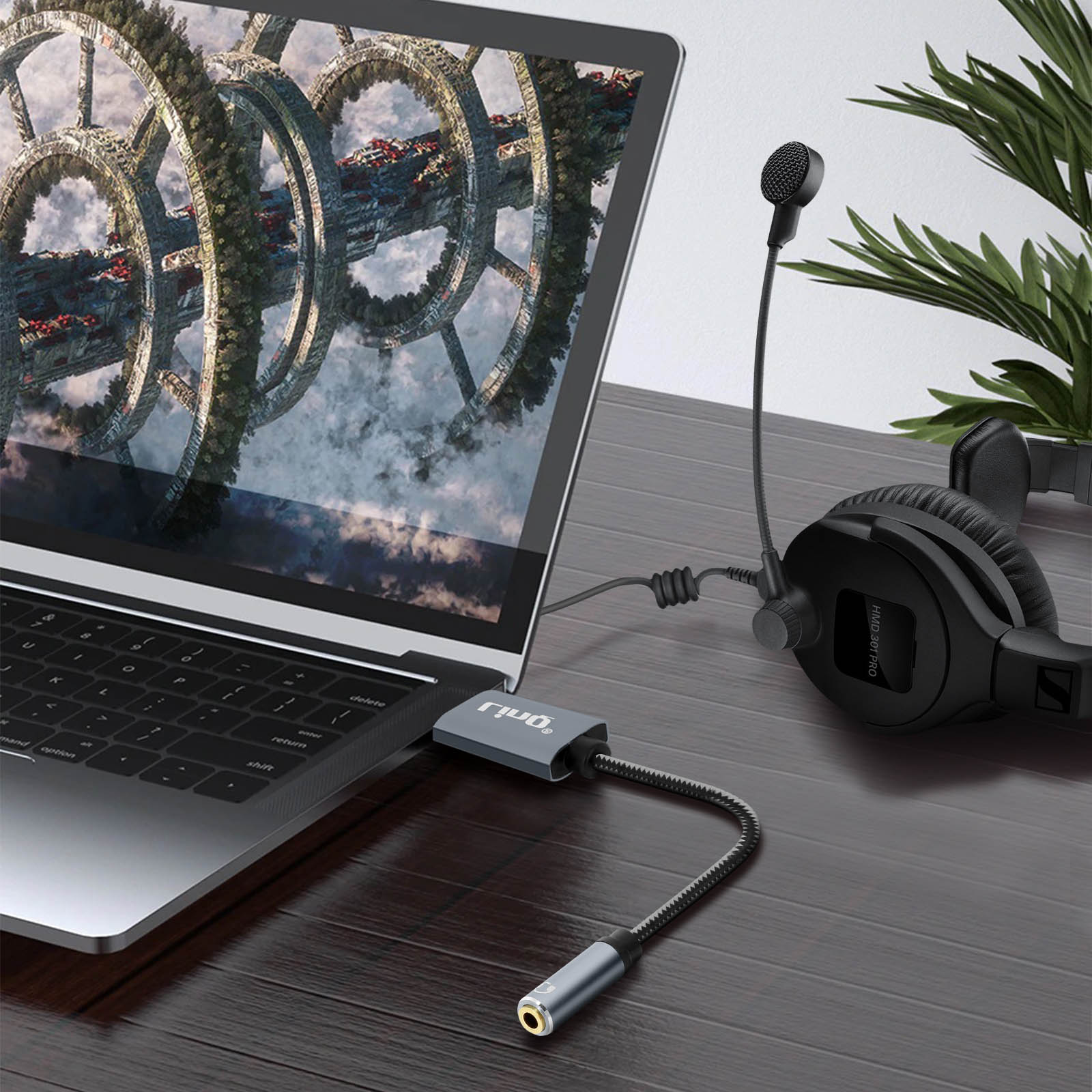 Laptop con cuffie, adattatore audio e microfono su una scrivania di legno.