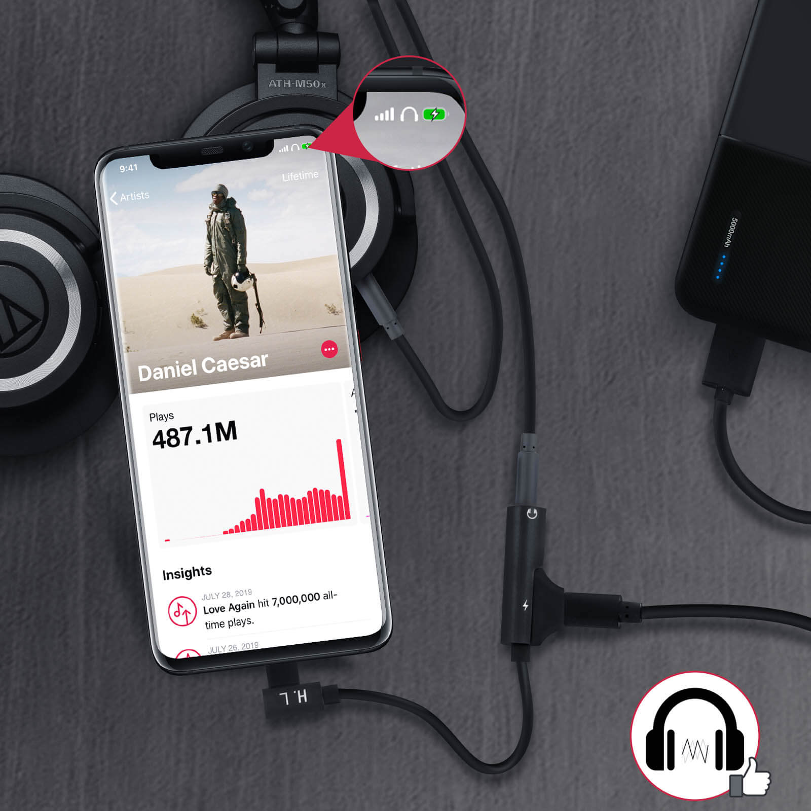 Smartphone con app de música, auriculares, cable de carga y banco de energía en superficie oscura.