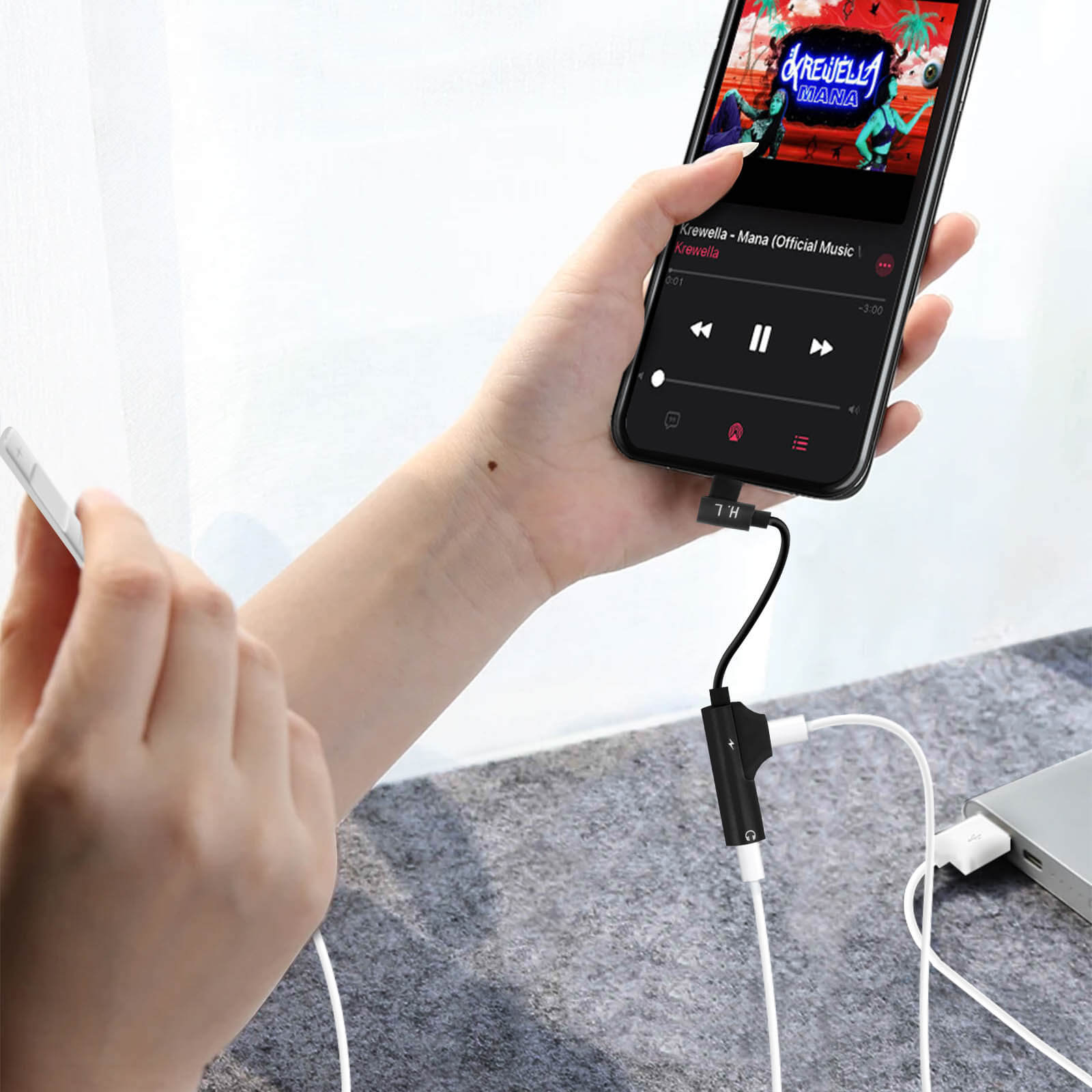 Una mano sostiene un teléfono conectado a un divisor de audio. Otro teléfono también conectado.