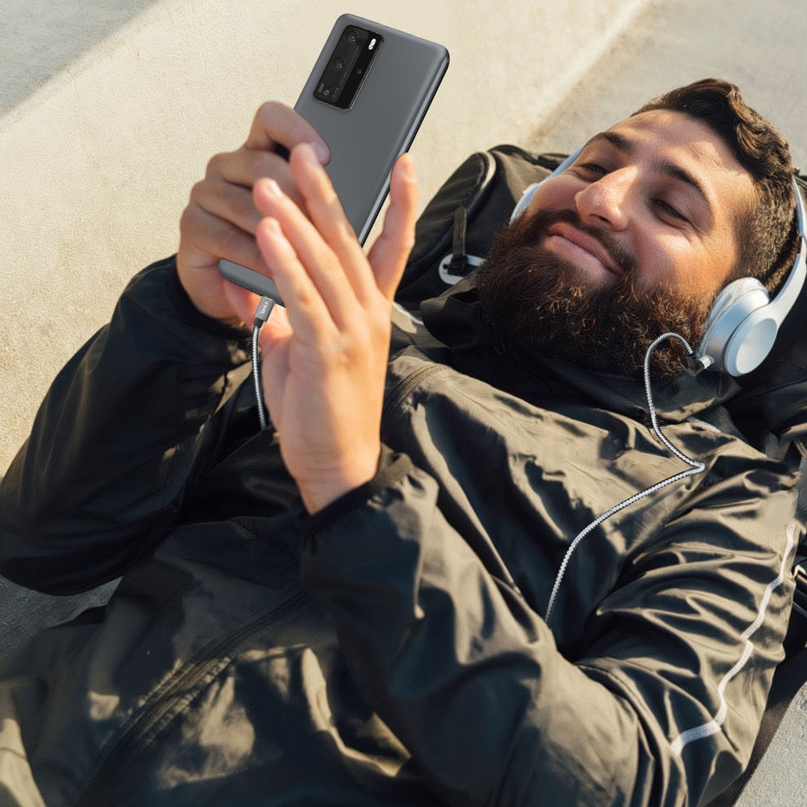 Hombre tumbado, usando un smartphone y con auriculares, al aire libre.