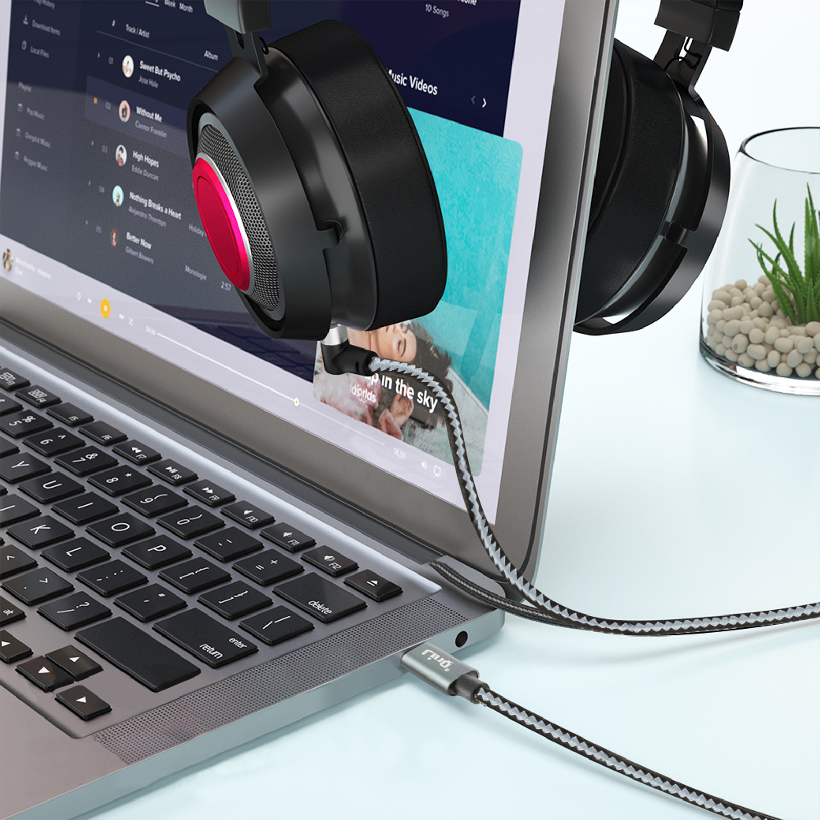 Portátil con auriculares enchufados por USB. Pantalla muestra interfaz de transmisión de música.