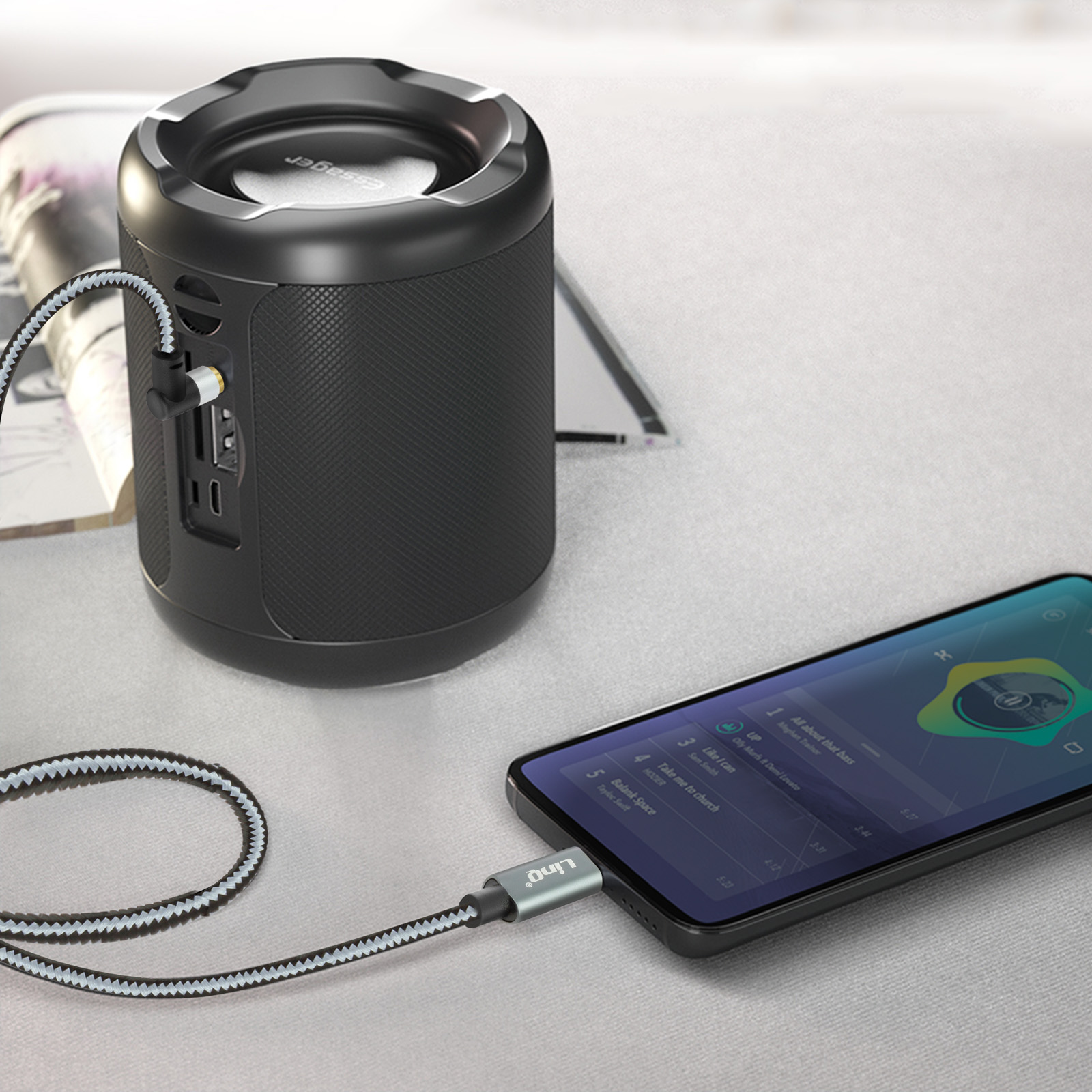 Un altavoz negro está conectado a un teléfono con un cable. El teléfono muestra una interfaz de música.