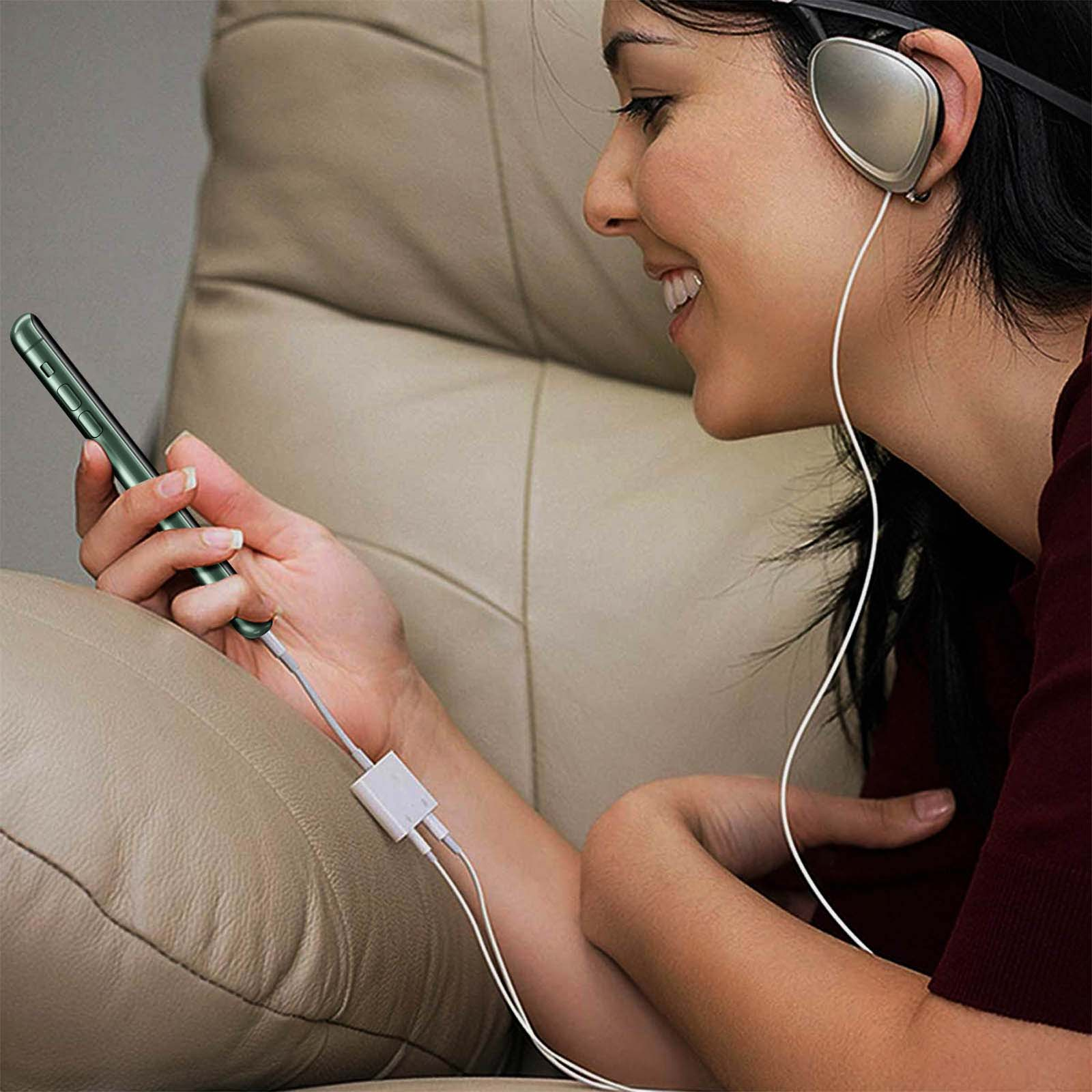 Femme utilisant un téléphone connecté à un casque. Elle sourit en se relaxant sur un canapé.
