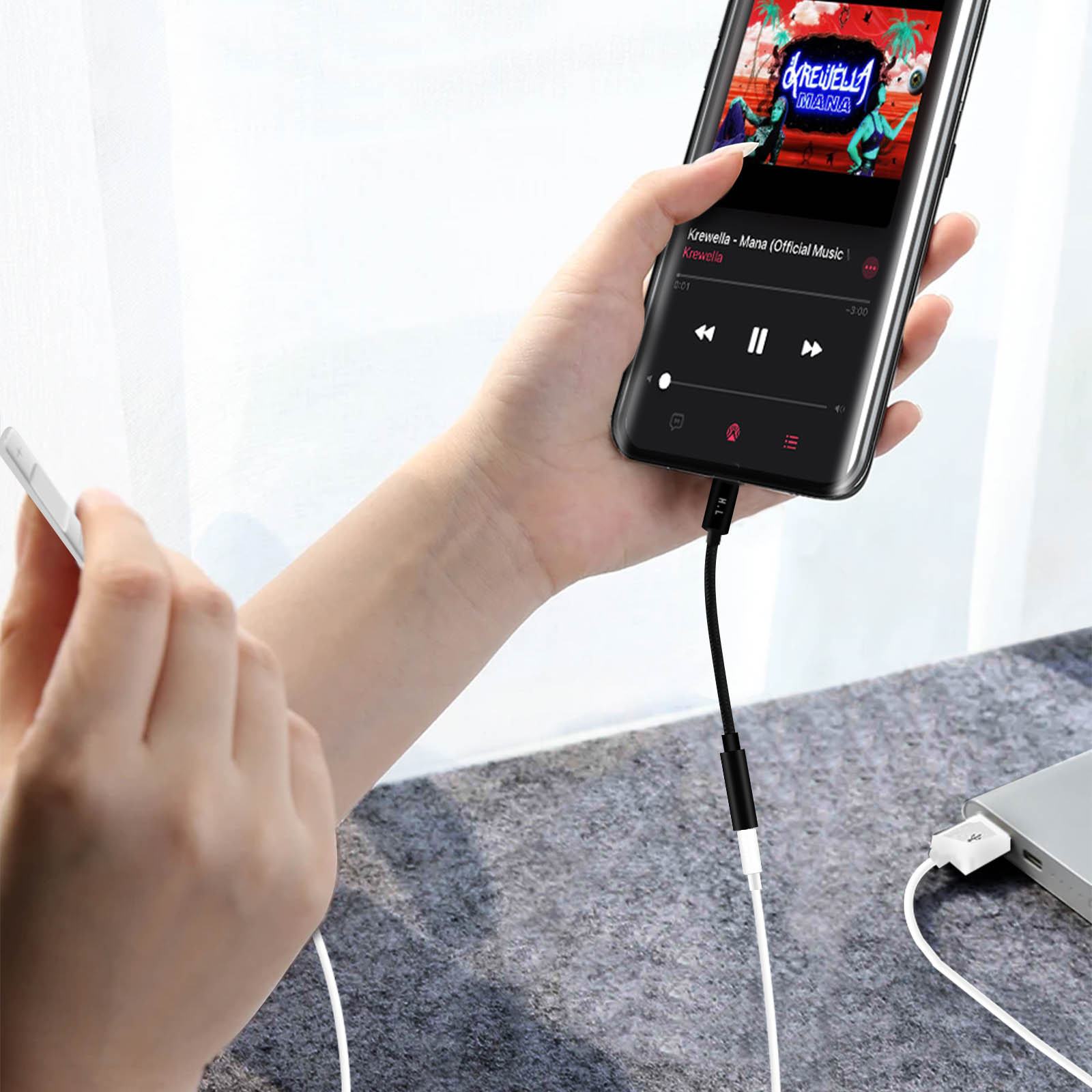 Una mano sosteniendo un teléfono reproduciendo música. El teléfono está conectado a un cable.