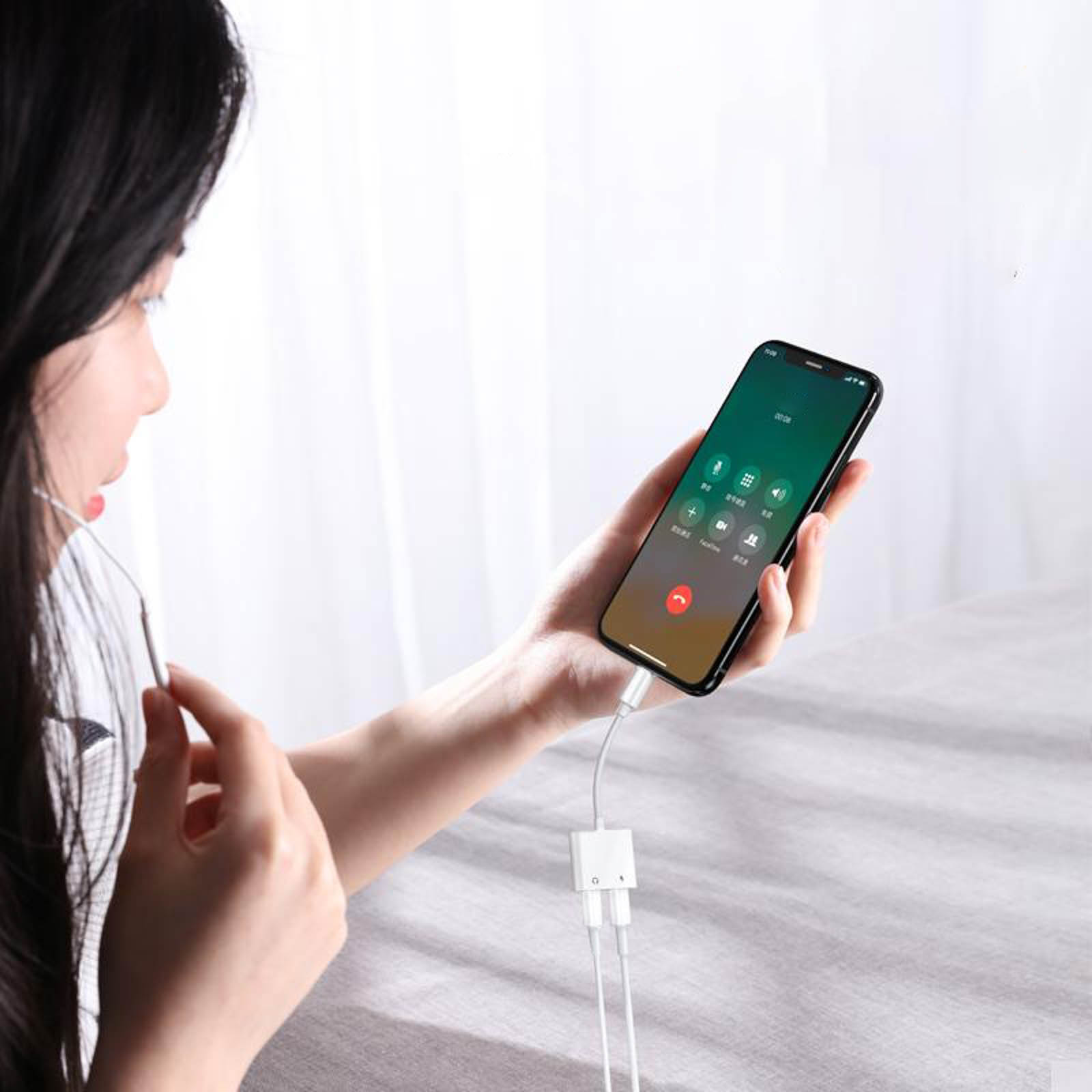 Una mujer sostiene un teléfono y está conectada a unos auriculares. Se muestra un adaptador de carga.