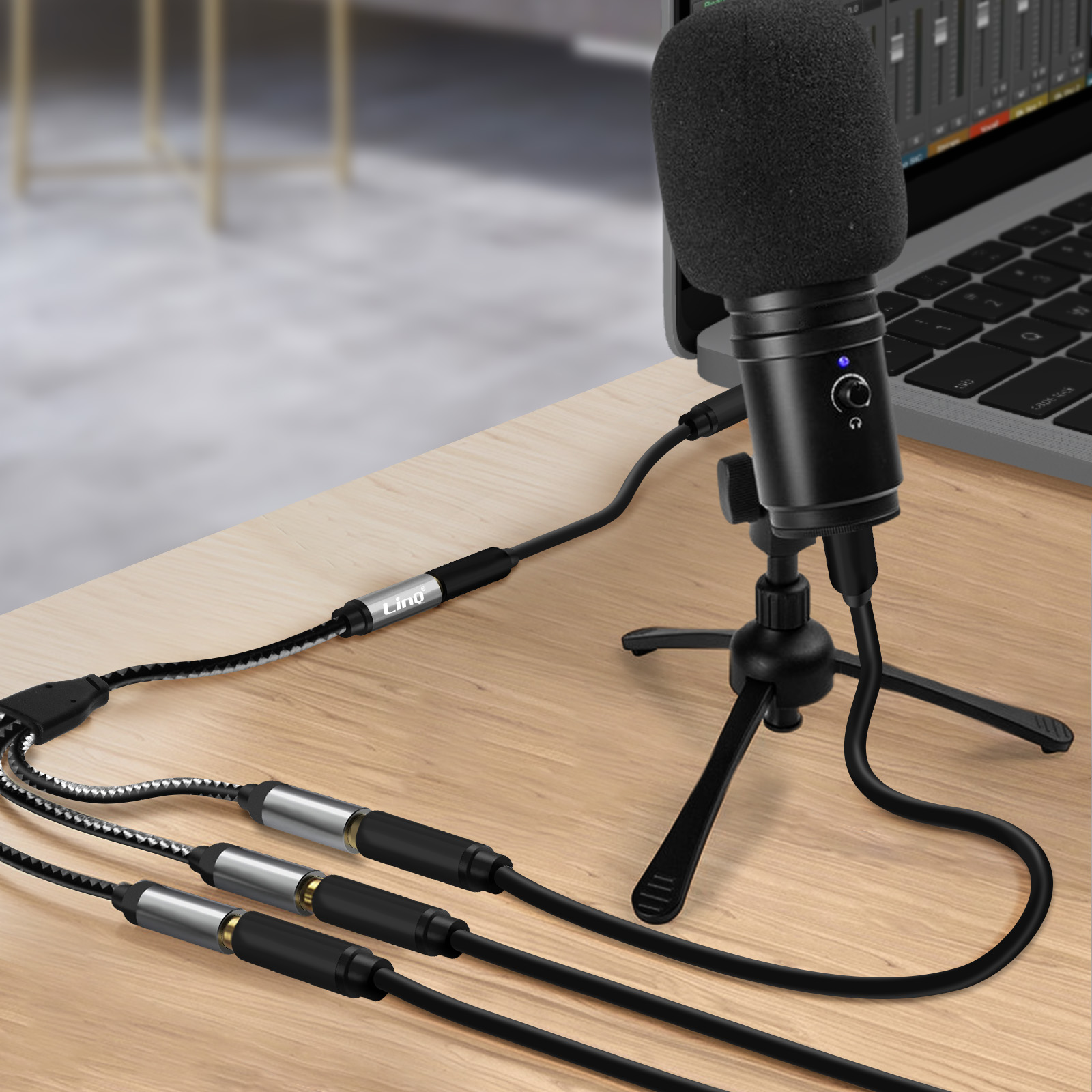 Schwarzes Mikrofon auf Stativ, verbunden mit Laptop, Kabel auf Holztisch.