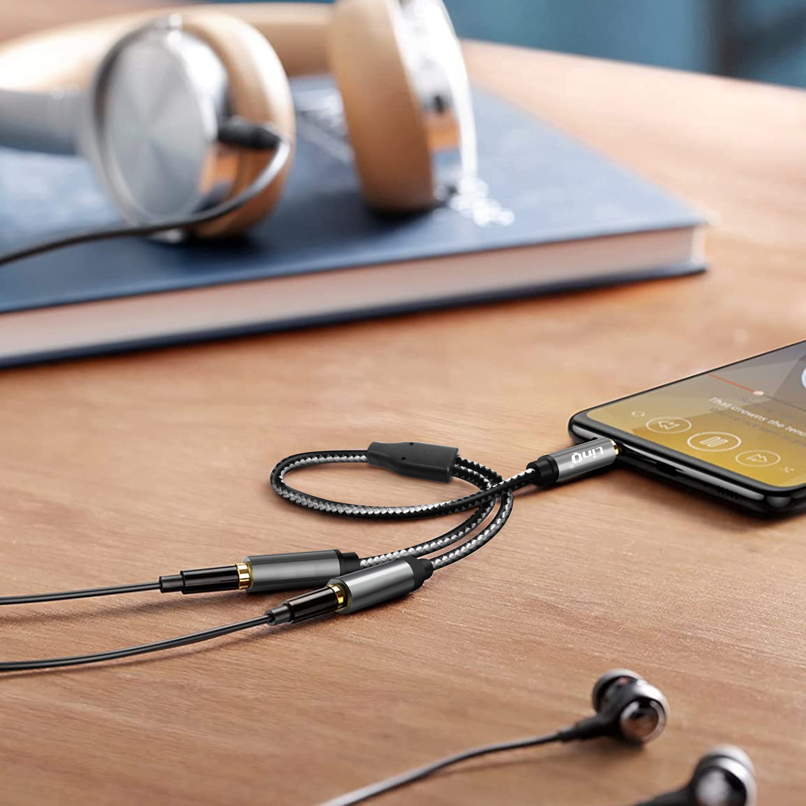 Un teléfono conectado a auriculares y otro cable, con libro y auriculares en la mesa.