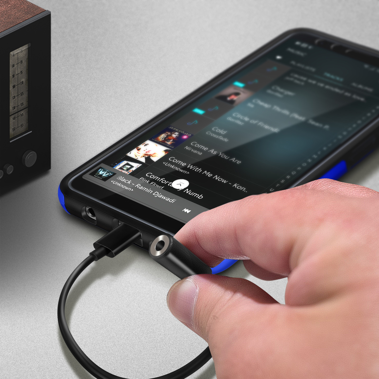Una mano enchufa un adaptador negro a un teléfono. El teléfono muestra una interfaz de aplicación de música.